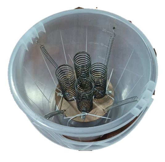 A top-down view of a plastic bucket with multiple metal springs inside, connected by wires, possibly part of a scientific or industrial setup.