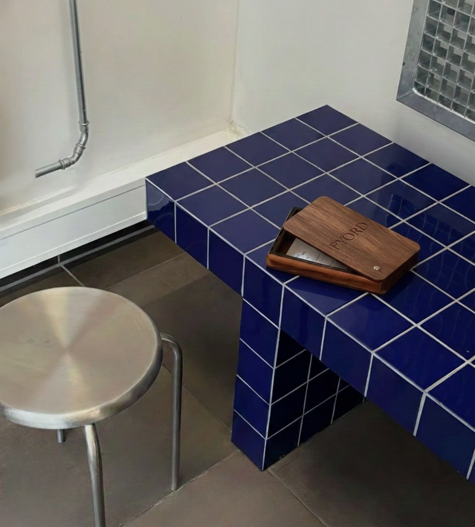 Ambiente interno com bancada de azulejos azuis, uma mesa de apoio de metal e uma parede com uma grade de ventilação