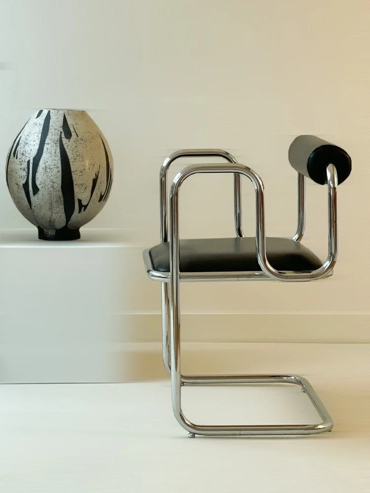 Uma cadeira de design moderno com estrutura de metal cromado e assento preto, ao lado de um vaso decorativo com padrão preto e branco.