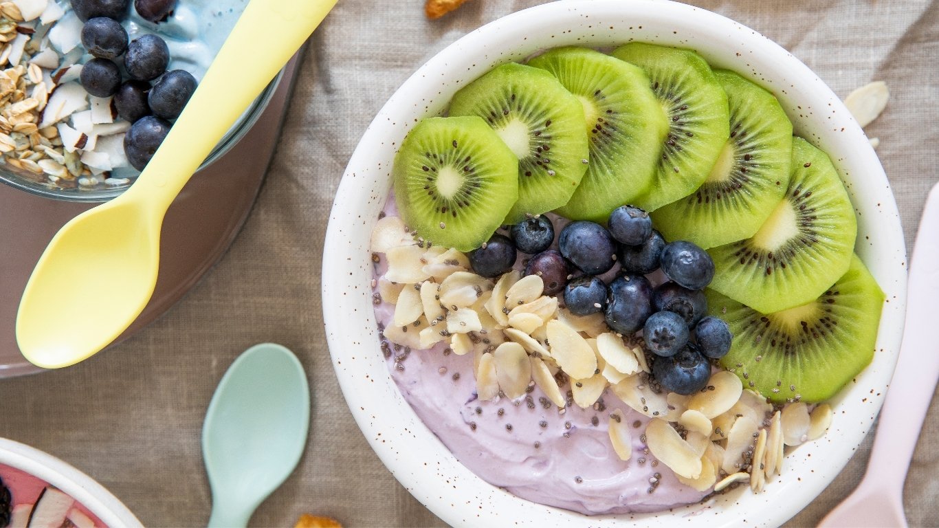 A bowl of yogurt topped with sliced kiwi, blueberries, sliced almonds, and chia seeds.