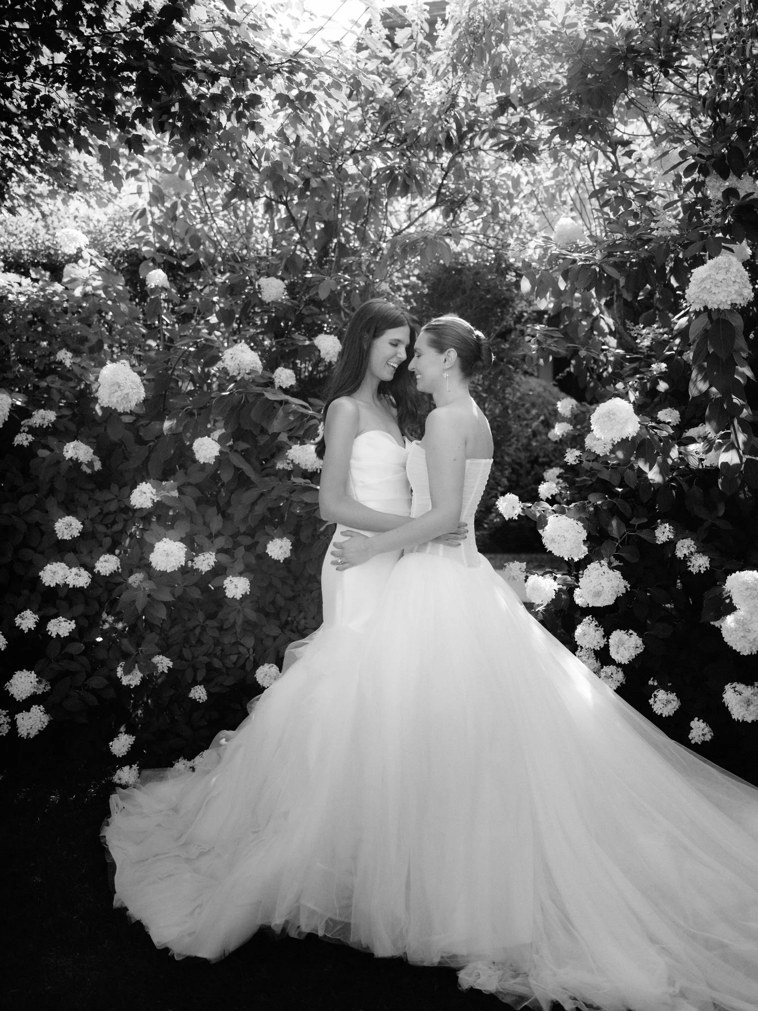 Two brides embracing in front of hydrangeas in a black and white portrait at Valley Rock Inn in Sloatsburg, photographed by Jenny Fu.