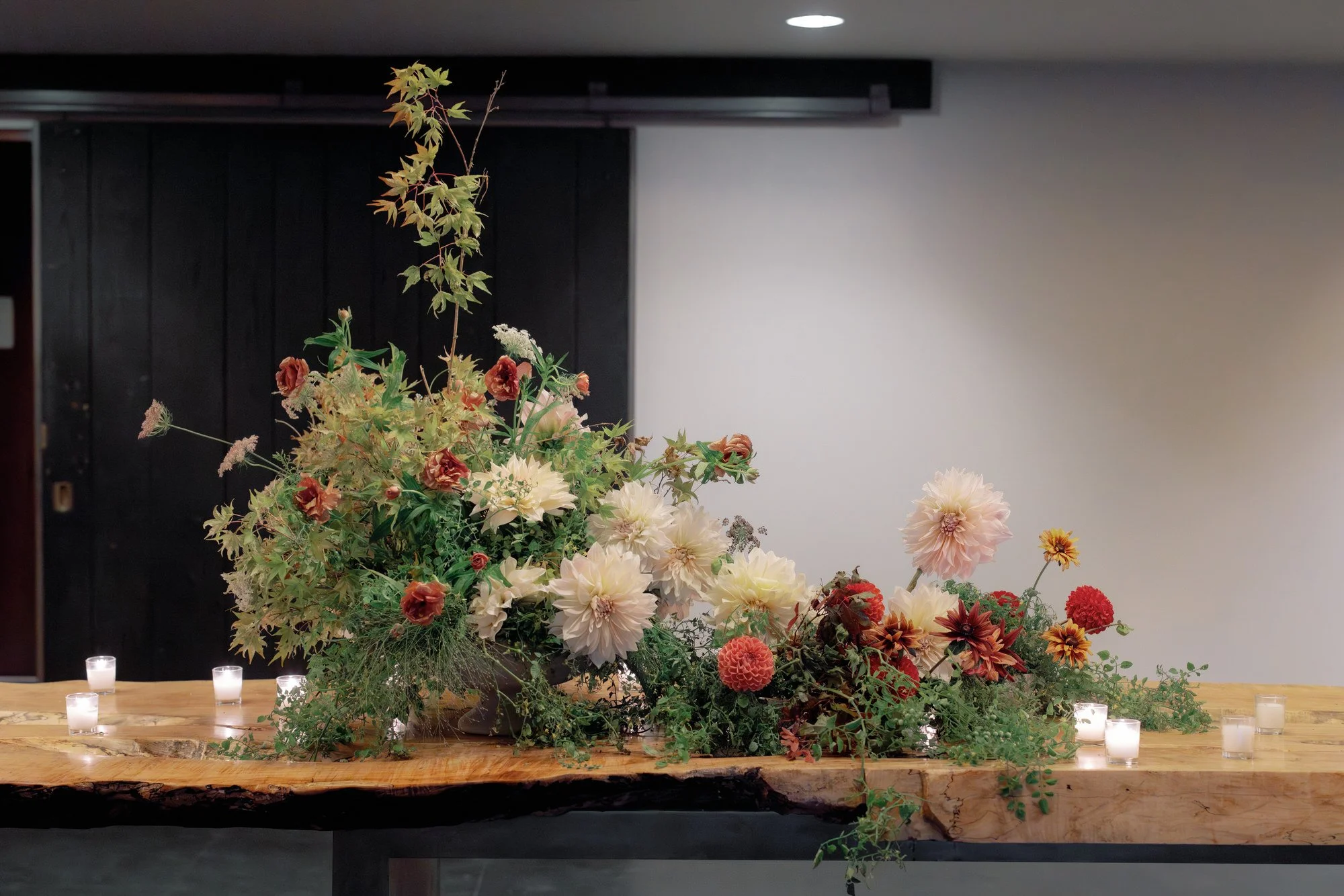 Lush garden arrangement on a live edge table with scattered votive candles at Blue Hill at Stone Barns, photographed by Jenny Fu.