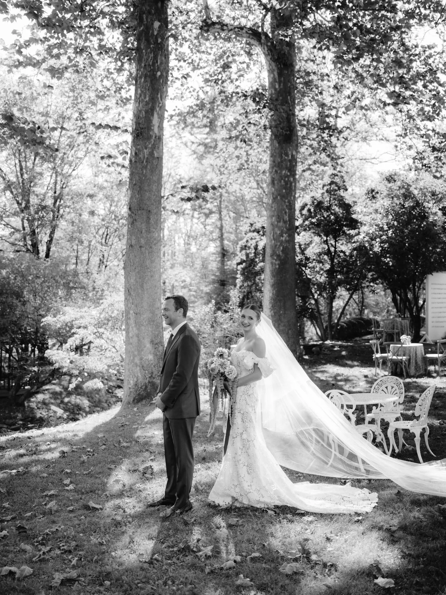 Bride smiling behind the groom just before the first look under tall trees at Troutbeck in Amenia, photographed by Jenny Fu.