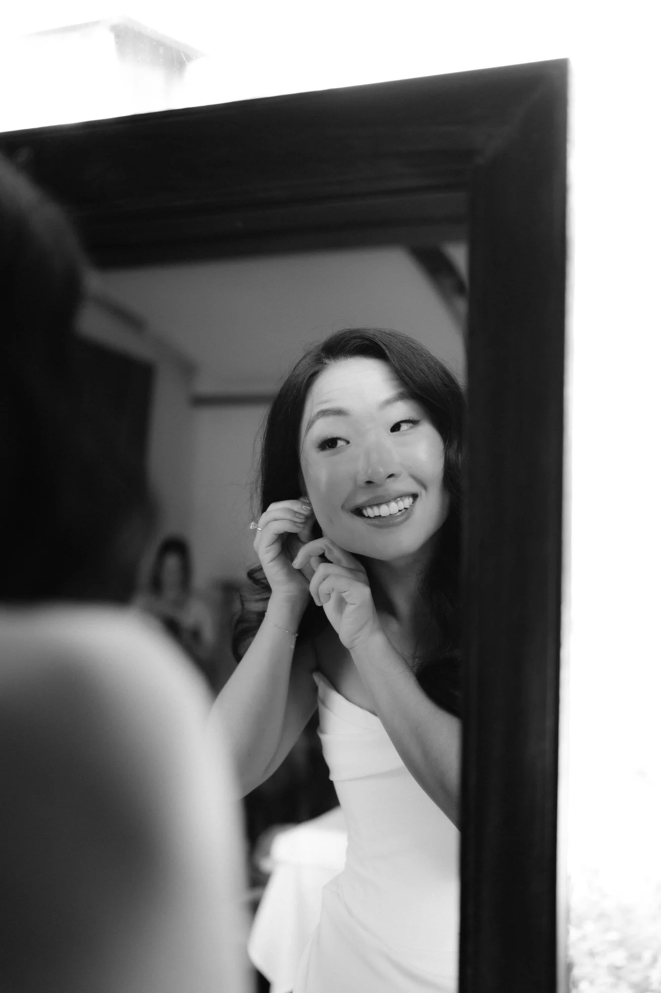 Bride adjusting her earring in the mirror in black and white before the ceremony at Blue Hill at Stone Barns, photographed by Jenny Fu.