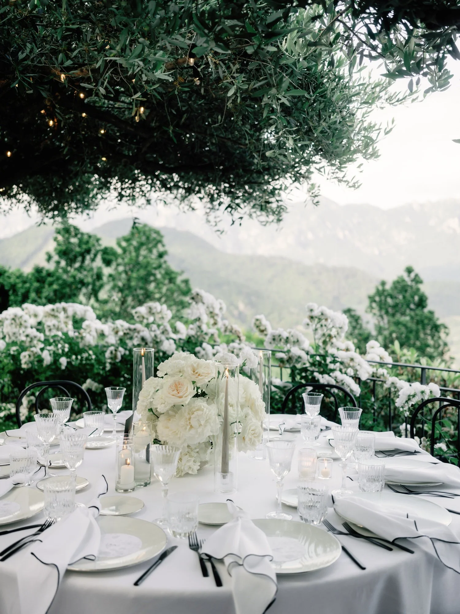 Elegant round dinner table set with white florals and candles overlooking the Amalfi Coast mountains at Caruso, A Belmond Hotel in Ravello, Italy, photographed by Jenny Fu.