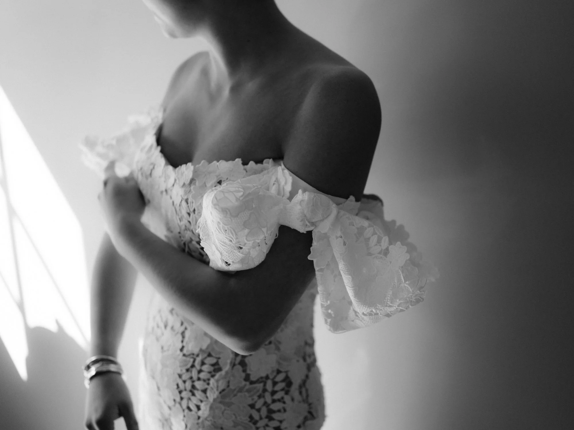 Cinematic detail of the bride adjusting her off-the-shoulder lace gown in soft window light at Troutbeck in Amenia, photographed by Jenny Fu.