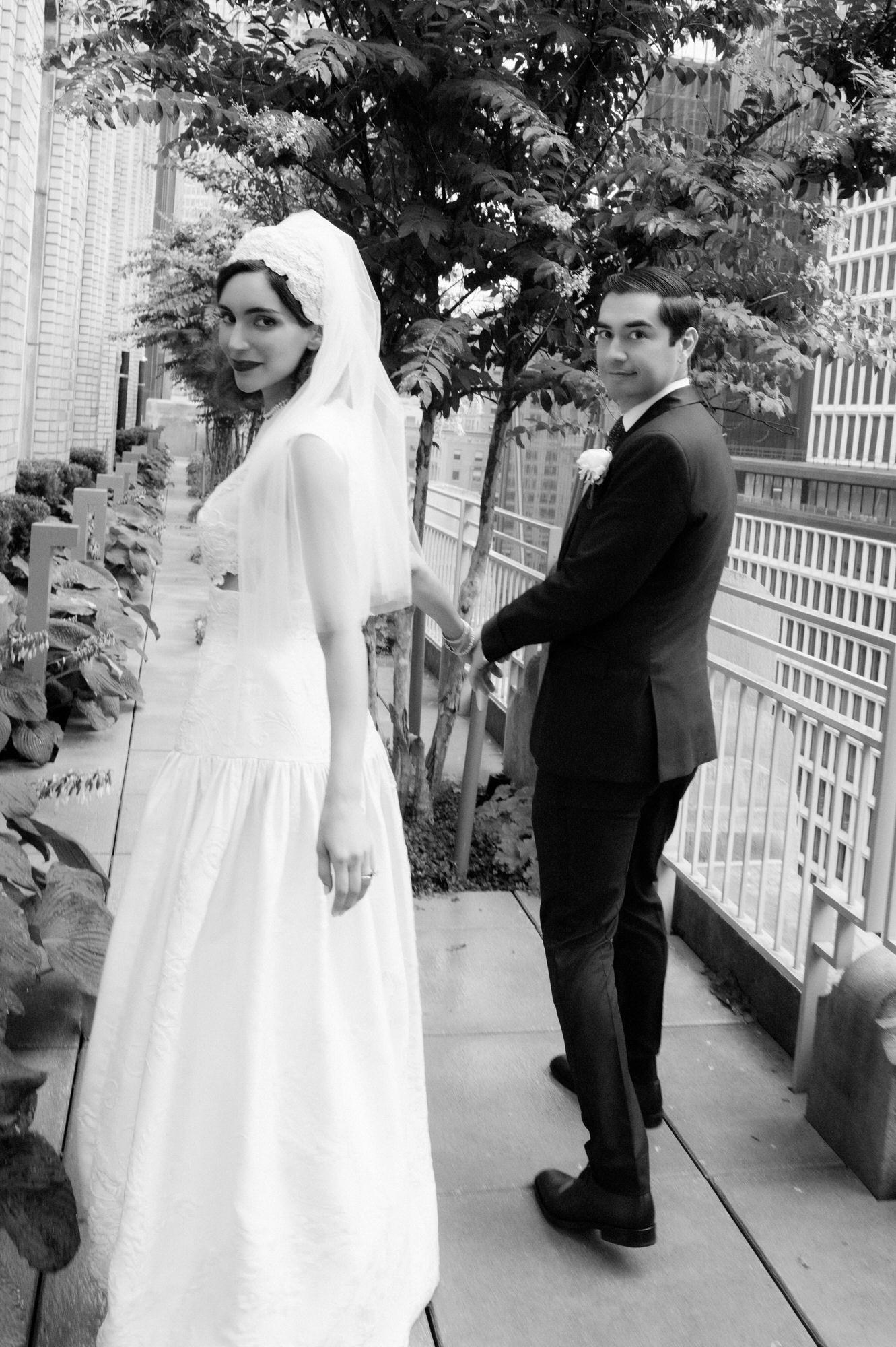 Black and white photo of the bride and groom glancing back as they walk along a terrace at the Waldorf Astoria New York, photographed by Jenny Fu.