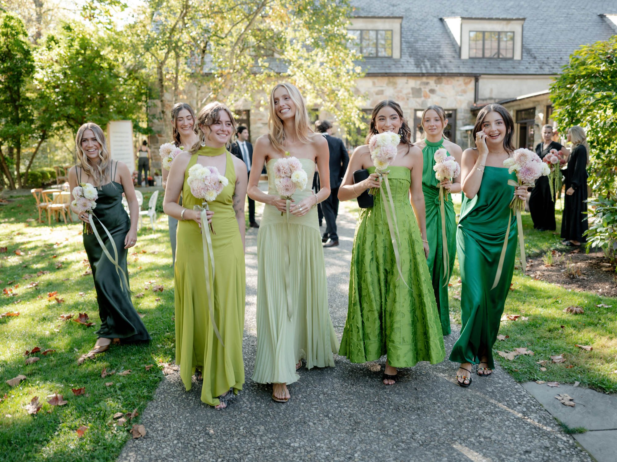 Bridesmaids in varying shades of green walking together with bouquets across the lawn at Troutbeck in Amenia, photographed by Jenny Fu.