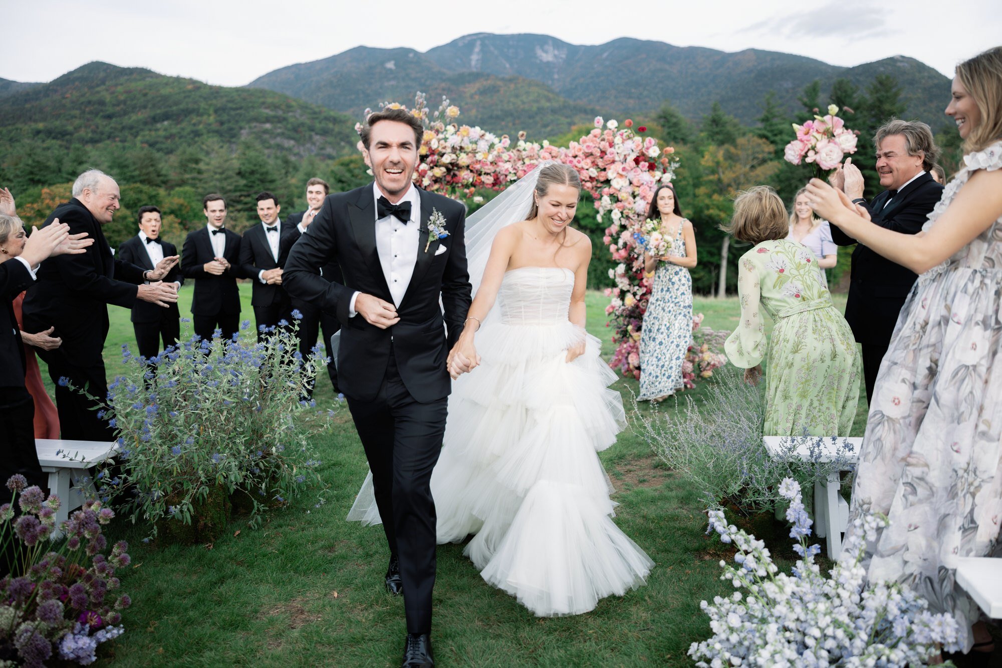 Bride and groom exit the ceremony joyfully while guests applaud at The Ausable Club in the Adirondacks