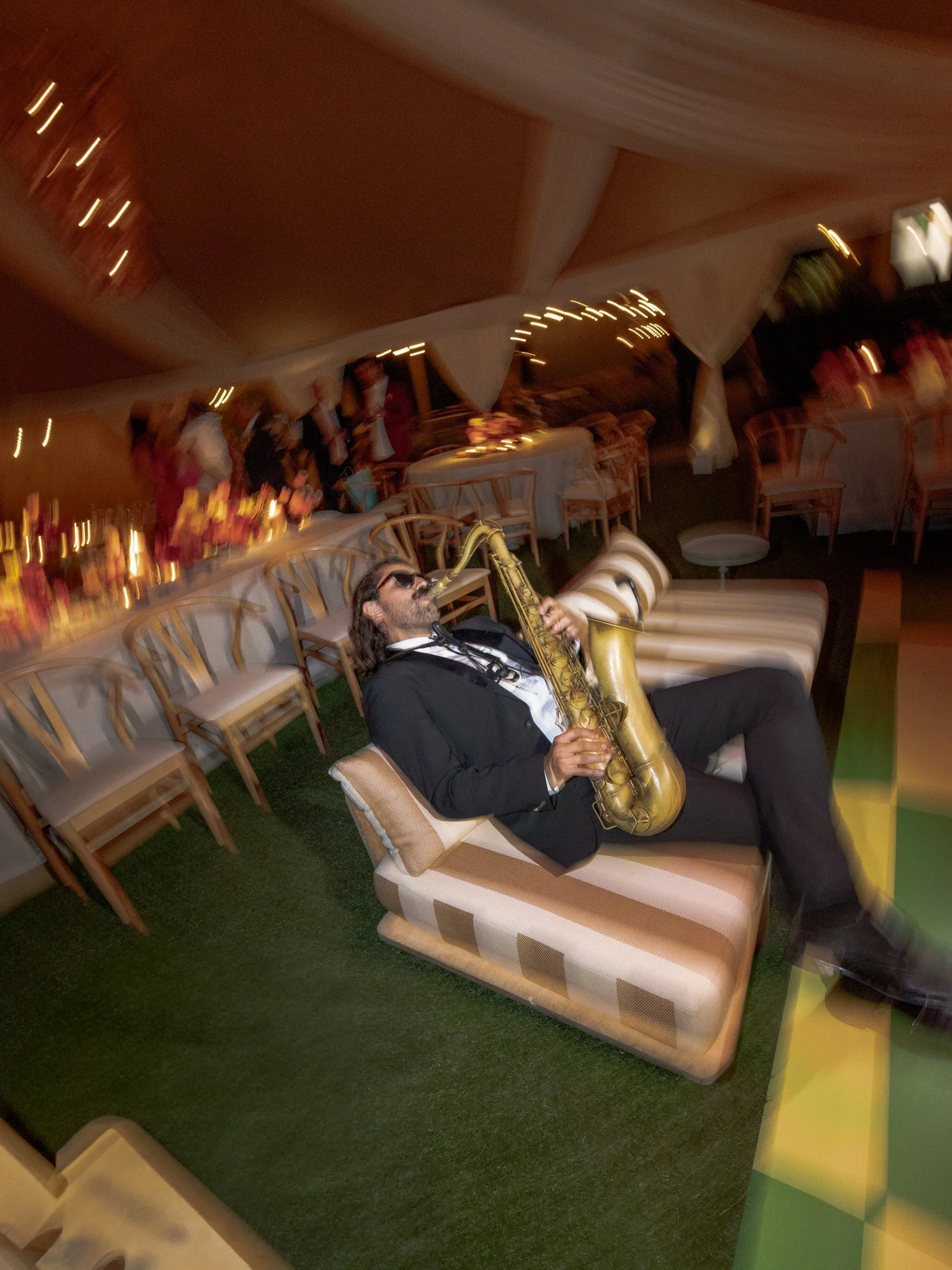 Saxophonist performing energetically while reclining on a striped lounge chair under the reception tent at Valley Rock Inn in Sloatsburg, photographed by Jenny Fu.