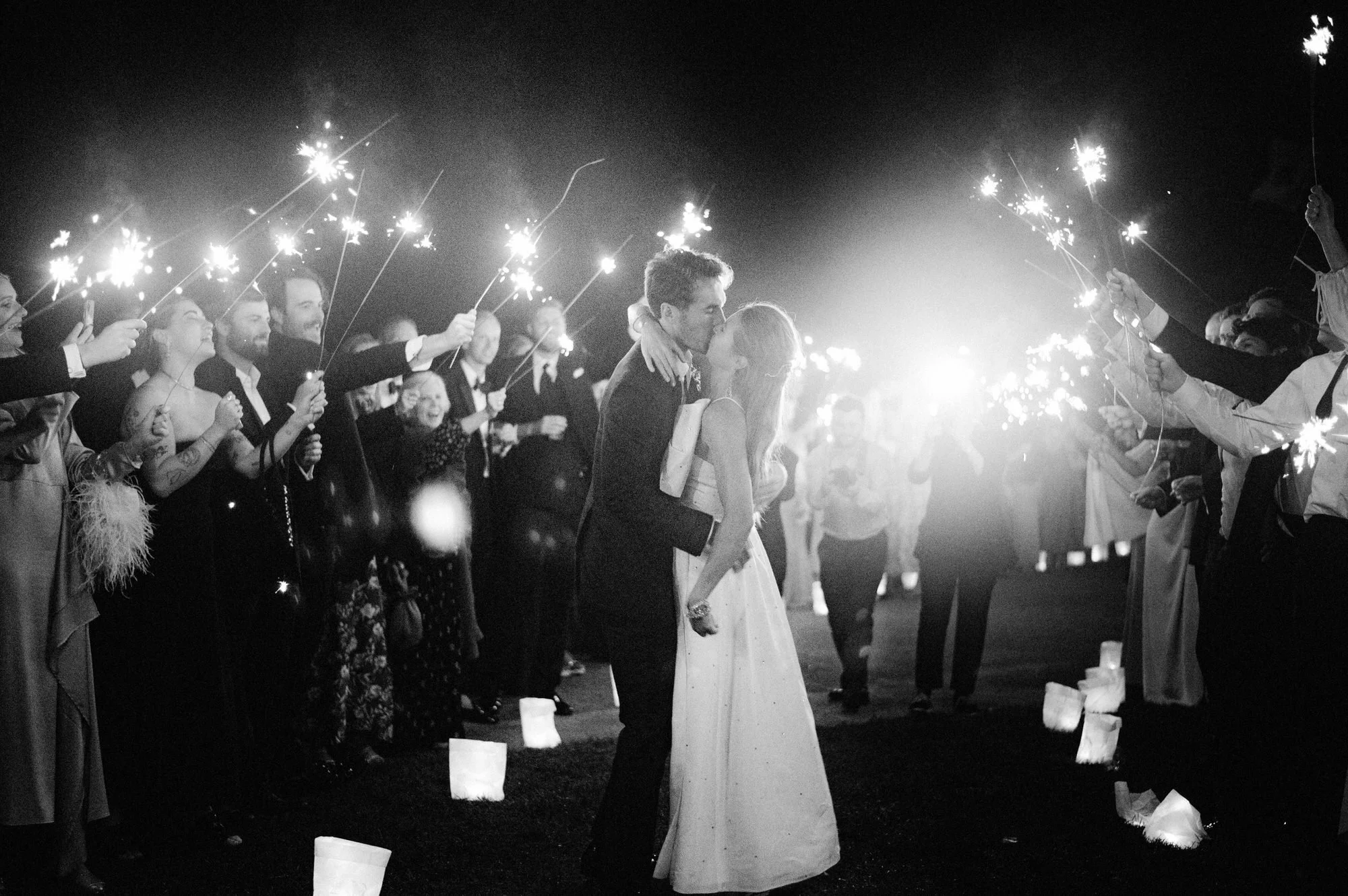 Bride and groom sharing a kiss under sparklers during their nighttime exit