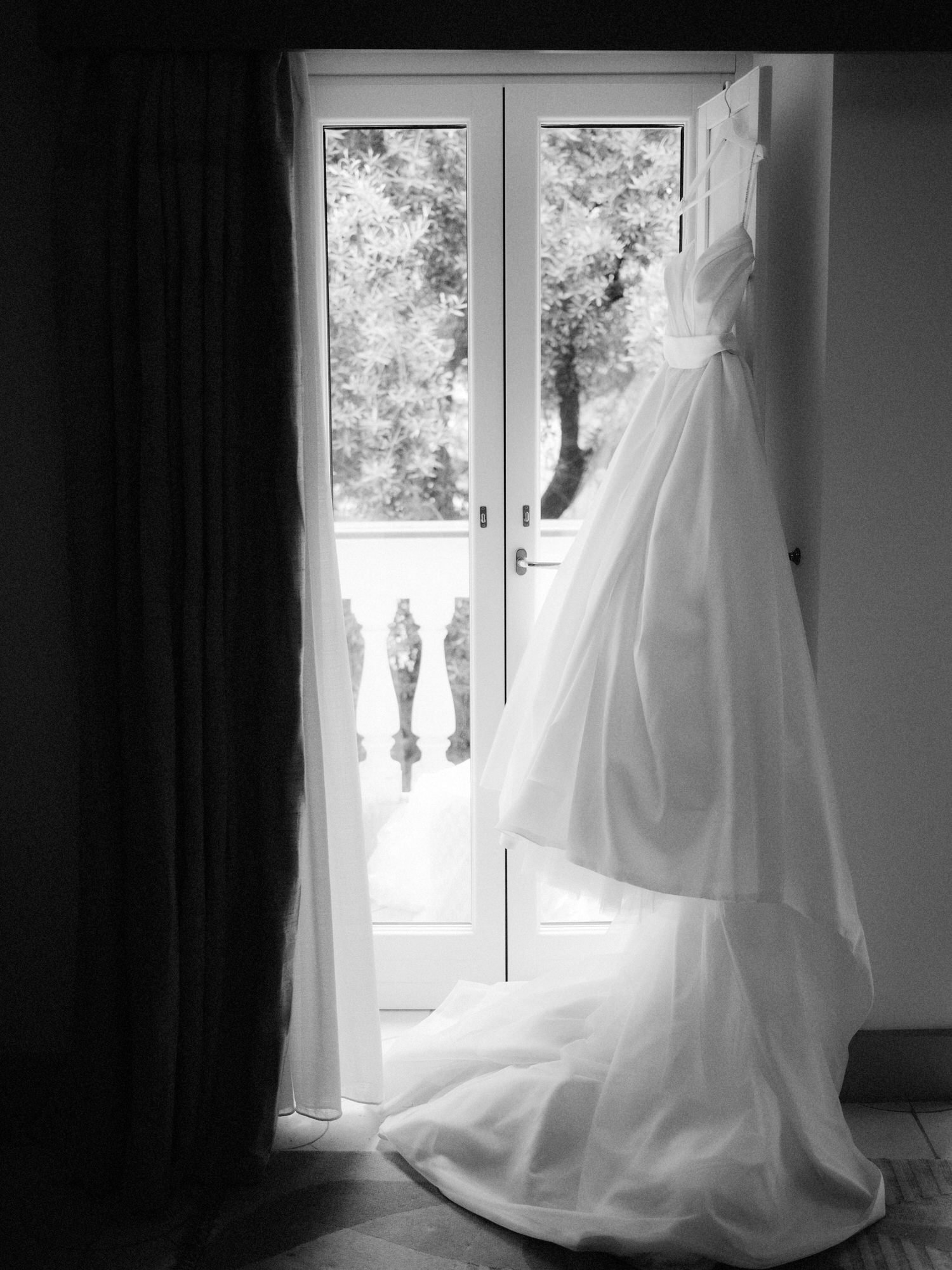 Elegant wedding gown hanging gracefully by French doors with garden views at Caruso, A Belmond Hotel in Ravello, Italy, photographed by Jenny Fu.