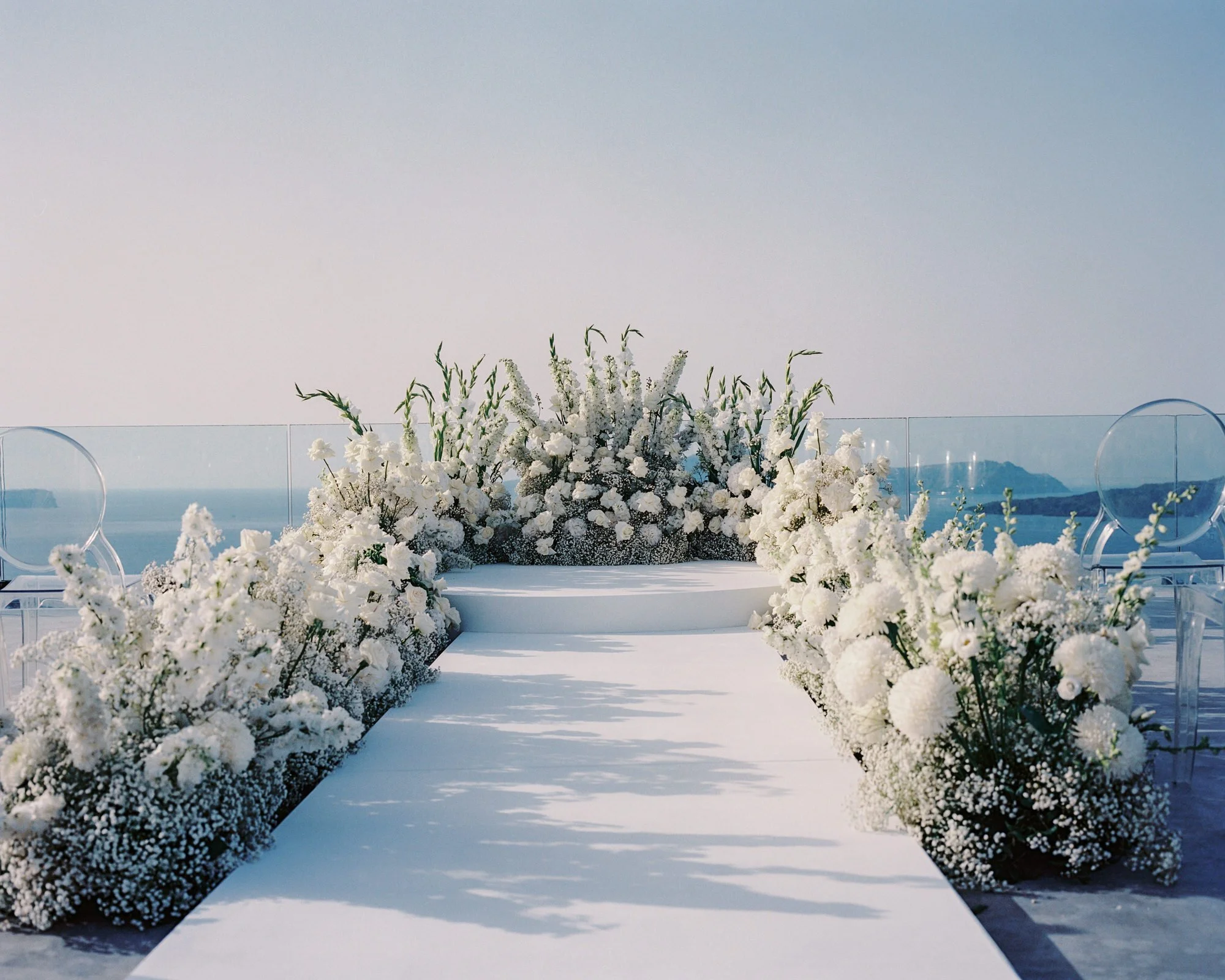 Elegant white floral aisle design at an oceanfront wedding ceremony with soft morning light, photographed by Jenny Fu.