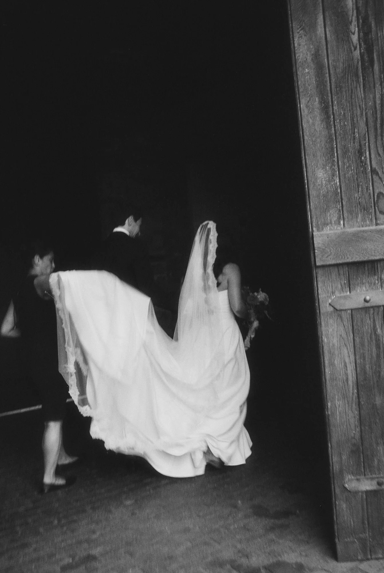 Bride and groom entering the barn as her cathedral veil trails behind in black and white at Blue Hill at Stone Barns, photographed by Jenny Fu.