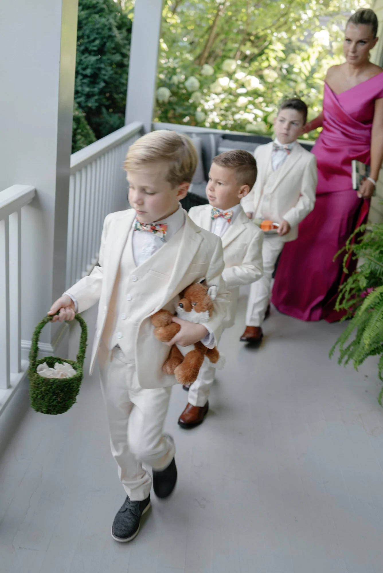 Ring bearers in cream suits walking down the porch carrying a moss basket and a stuffed fox at Valley Rock Inn in Sloatsburg, photographed by Jenny Fu.