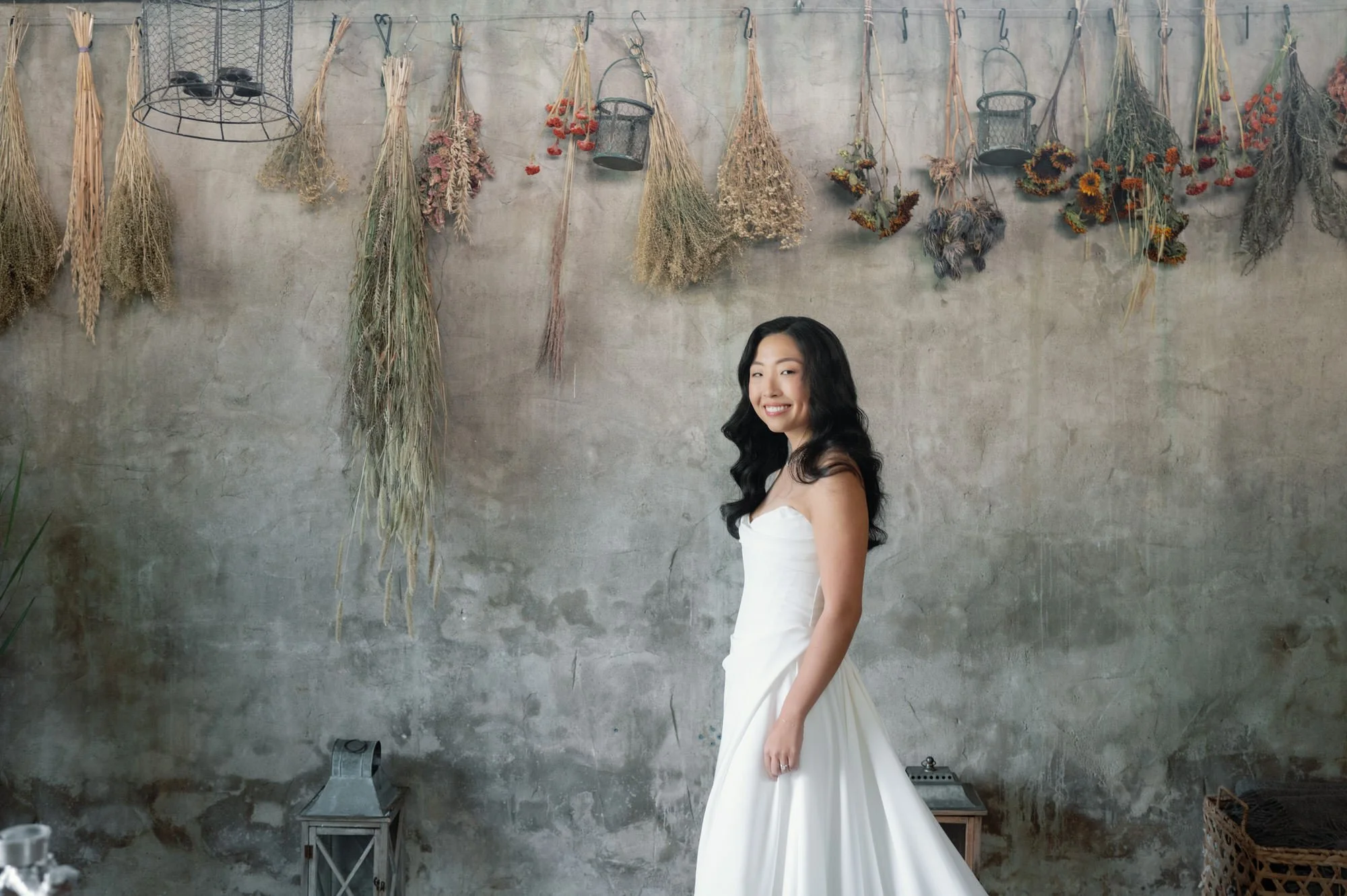 Bride smiling in the herb drying room with bundles of botanicals along the wall at Blue Hill at Stone Barns, photographed by Jenny Fu.