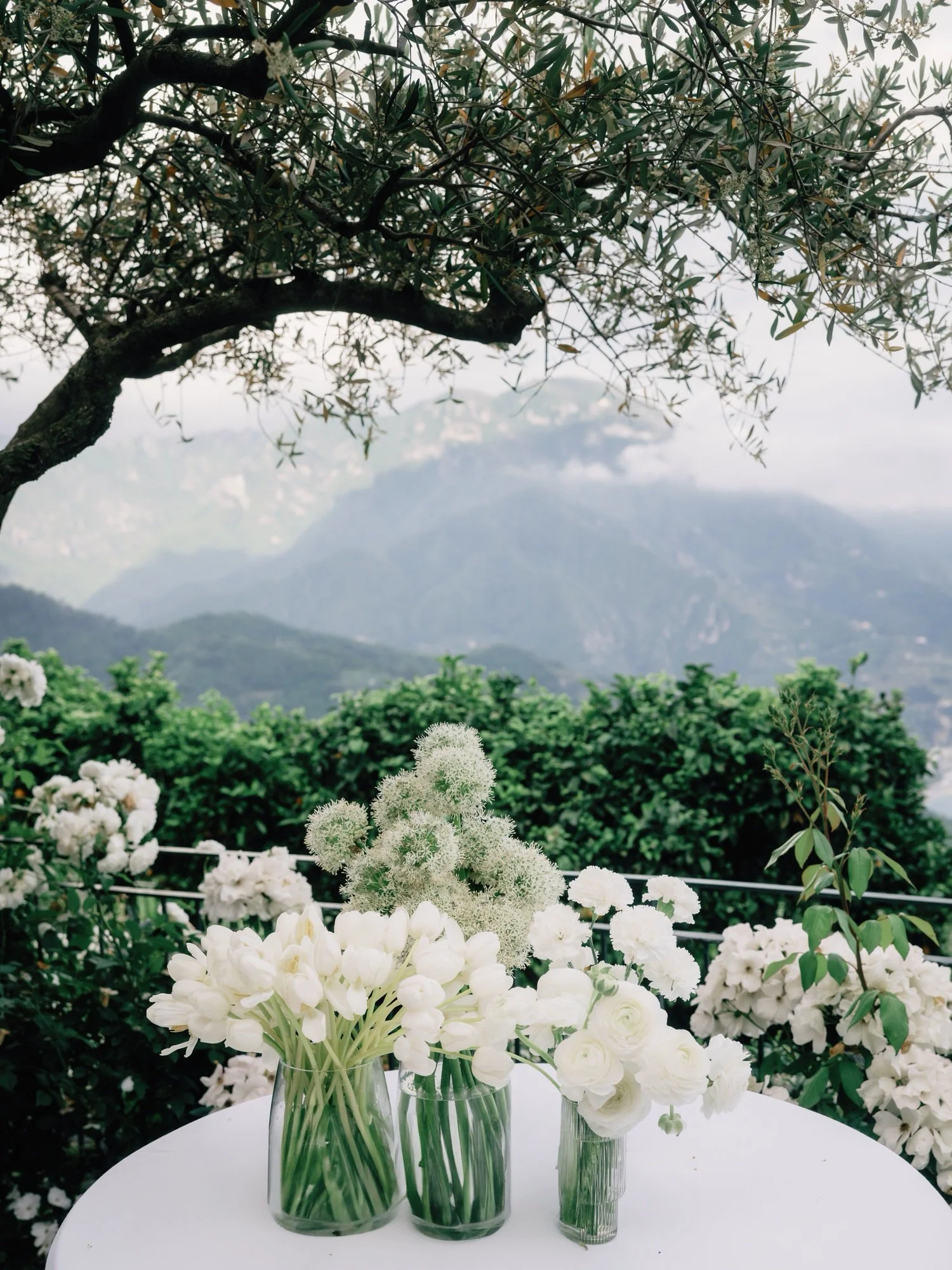 Evening dinner reception setup beneath olive trees with white linens and floral arrangements at Caruso, A Belmond Hotel in Ravello, Italy, photographed by Jenny Fu.