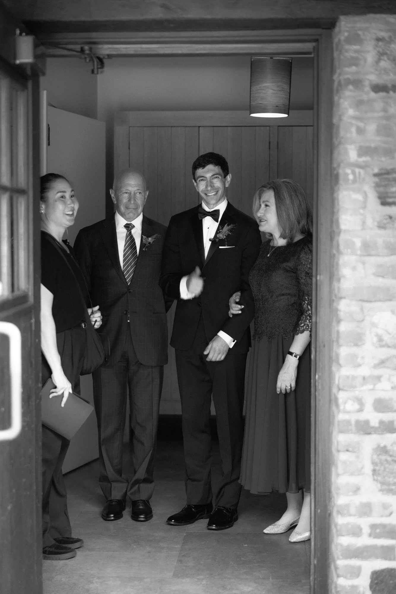 Candid moment of the groom with his parents and officiant framed in the doorway in black and white at Blue Hill at Stone Barns, photographed by Jenny Fu.