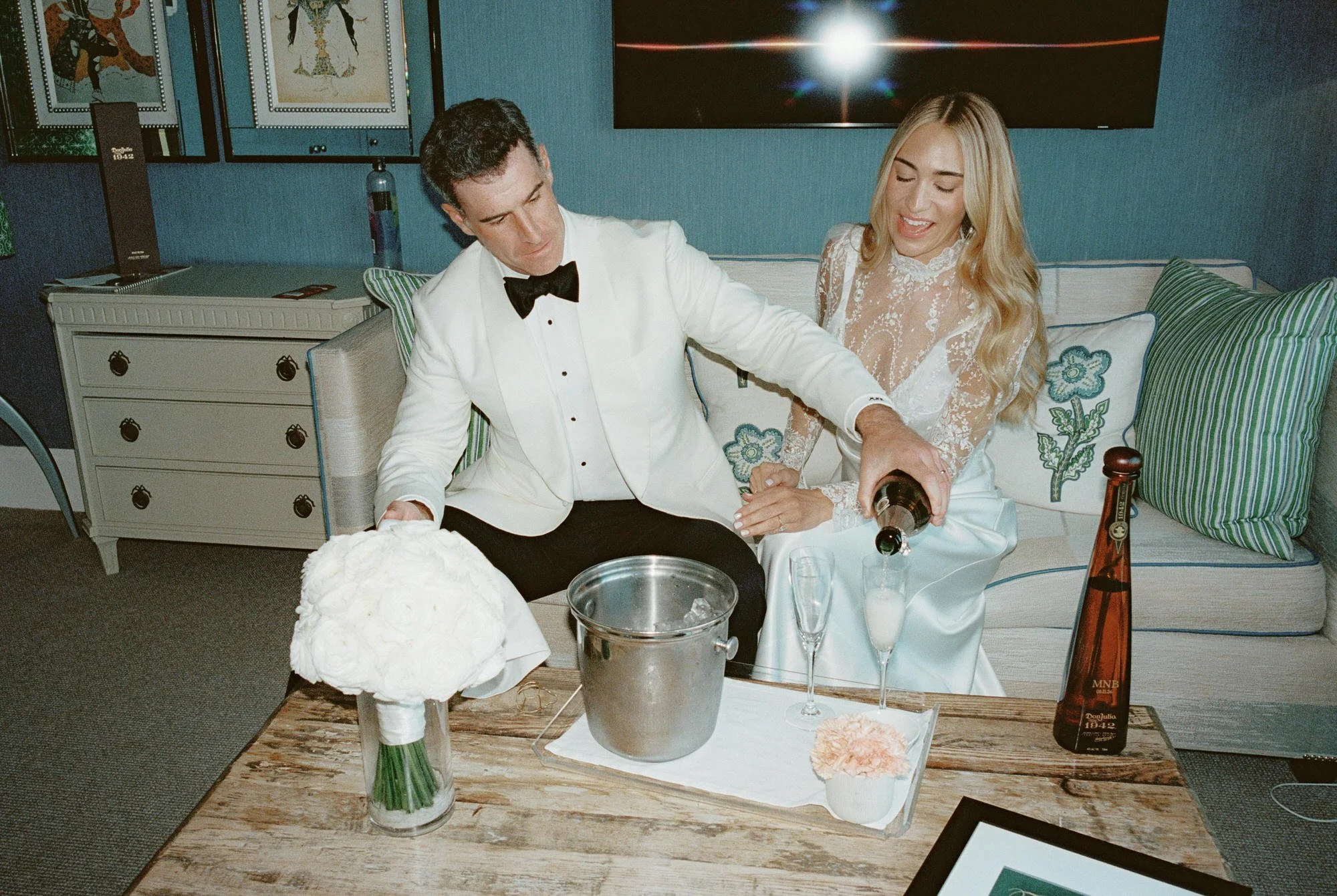 Couple pouring champagne together in their hotel suite surrounded by flowers and candlelight at Crosby Street Hotel in Soho, photographed by Jenny Fu.