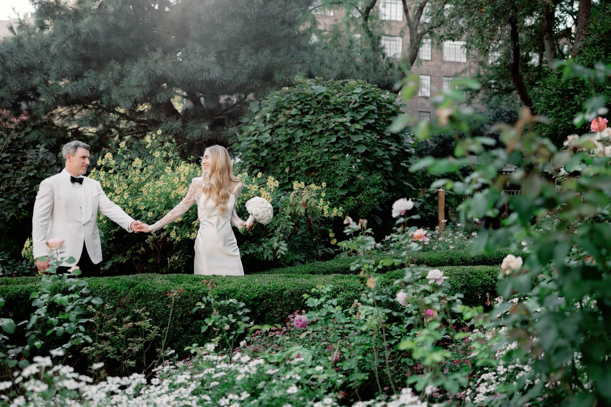 Bride and groom walking hand in hand along the winding garden path at Jefferson Market Garden in the West Village, photographed by Jenny Fu.