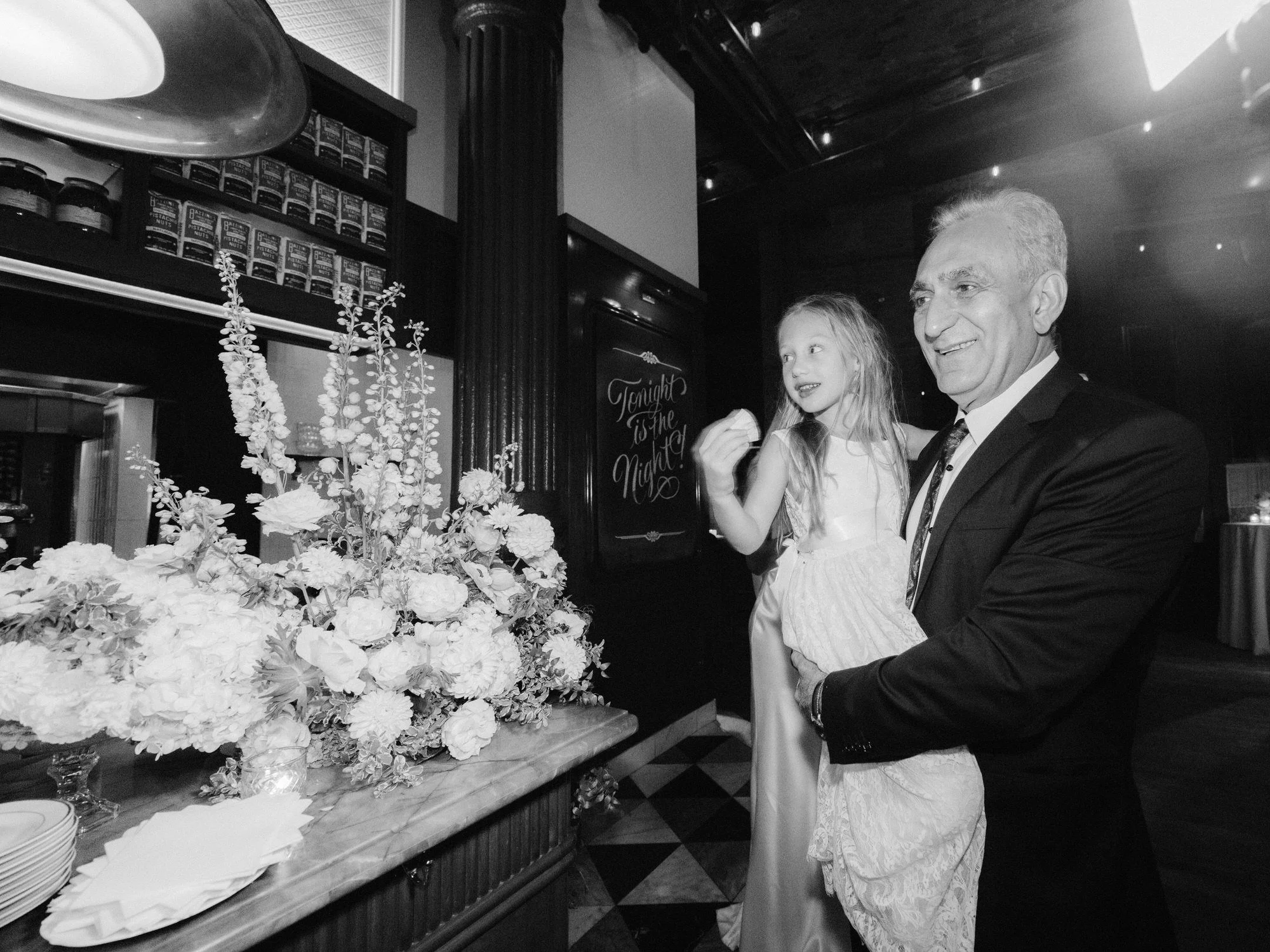 Father holding his young daughter near floral arrangements during dessert hour at Torrisi in Manhattan, photographed by Jenny Fu.