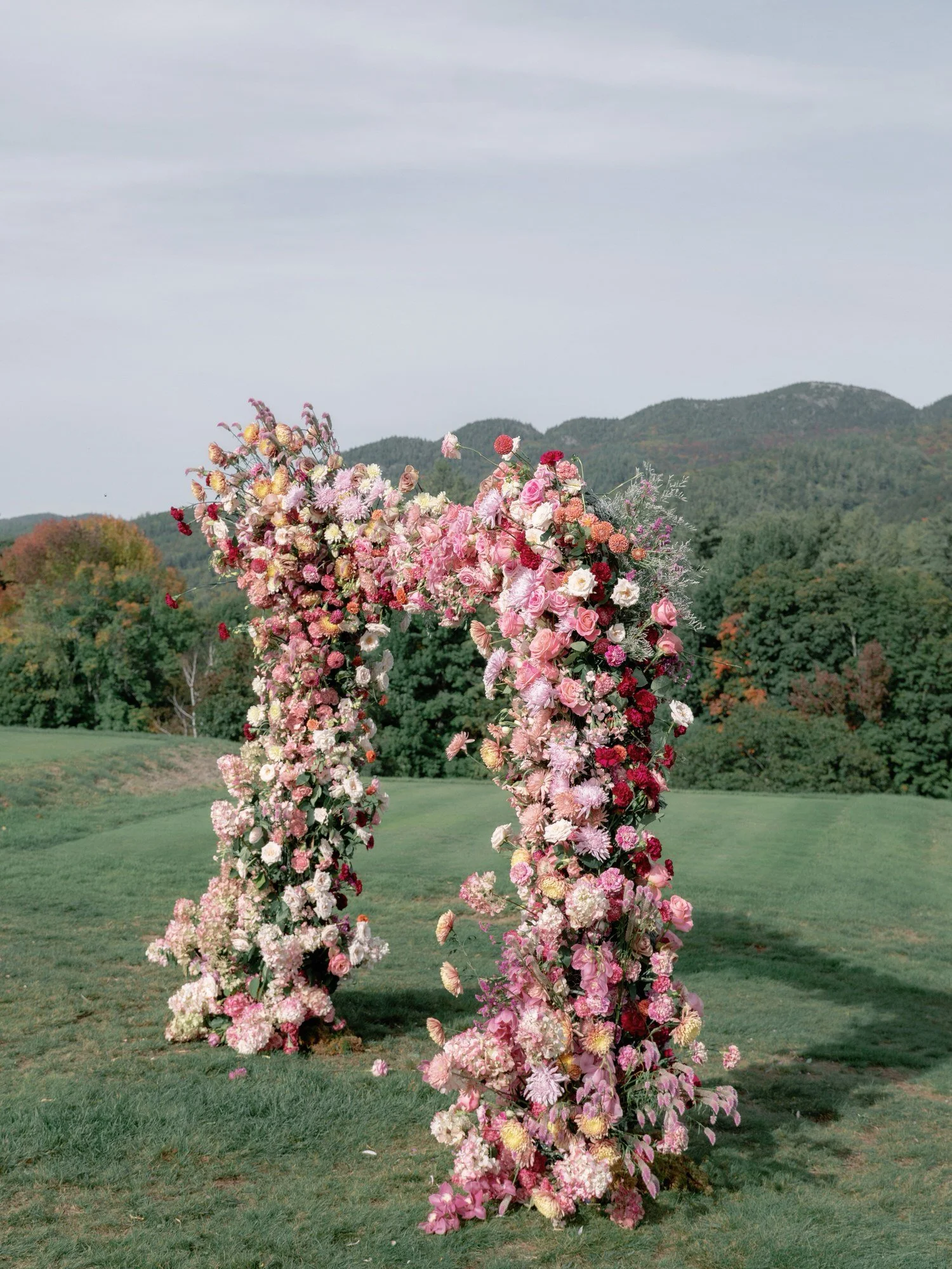 Ceremony floral arch with pink and red blooms against the mountain backdrop at the Ausable Club in the Adirondacks