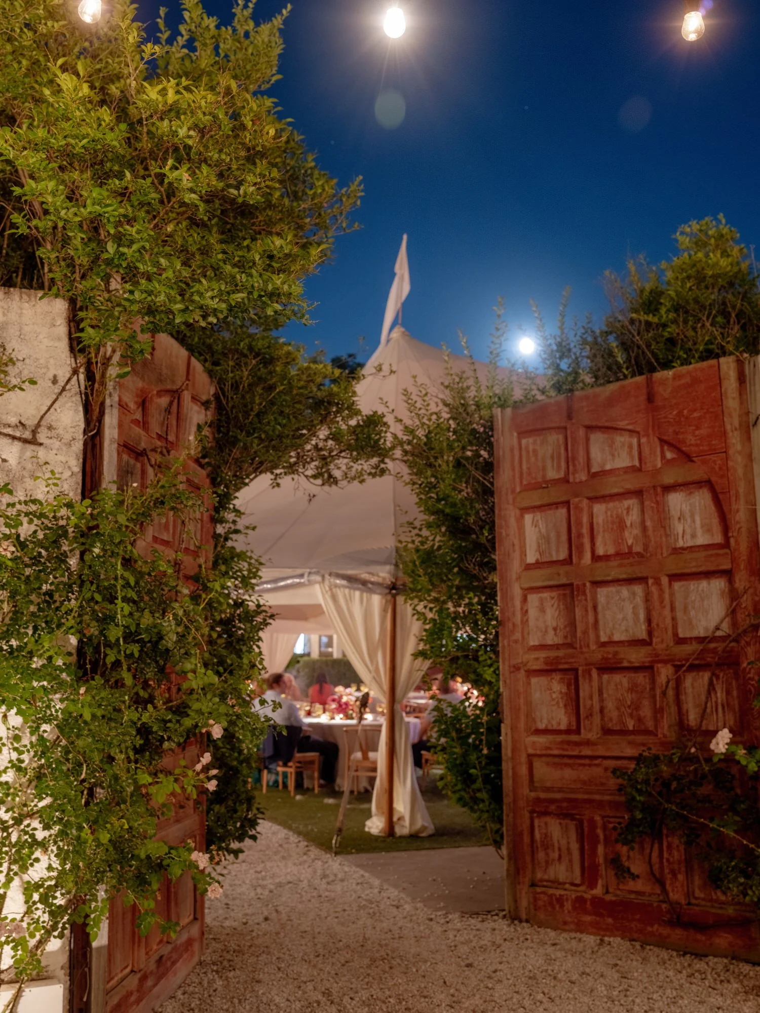View through open wooden doors into the glowing nighttime wedding reception with string lights at Valley Rock Inn in Sloatsburg, photographed by Jenny Fu.