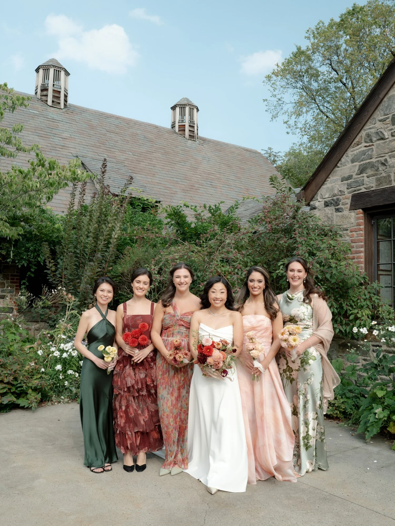 Bride standing with her bridesmaids in mixed floral and satin dresses in the courtyard at Blue Hill at Stone Barns, photographed by Jenny Fu.