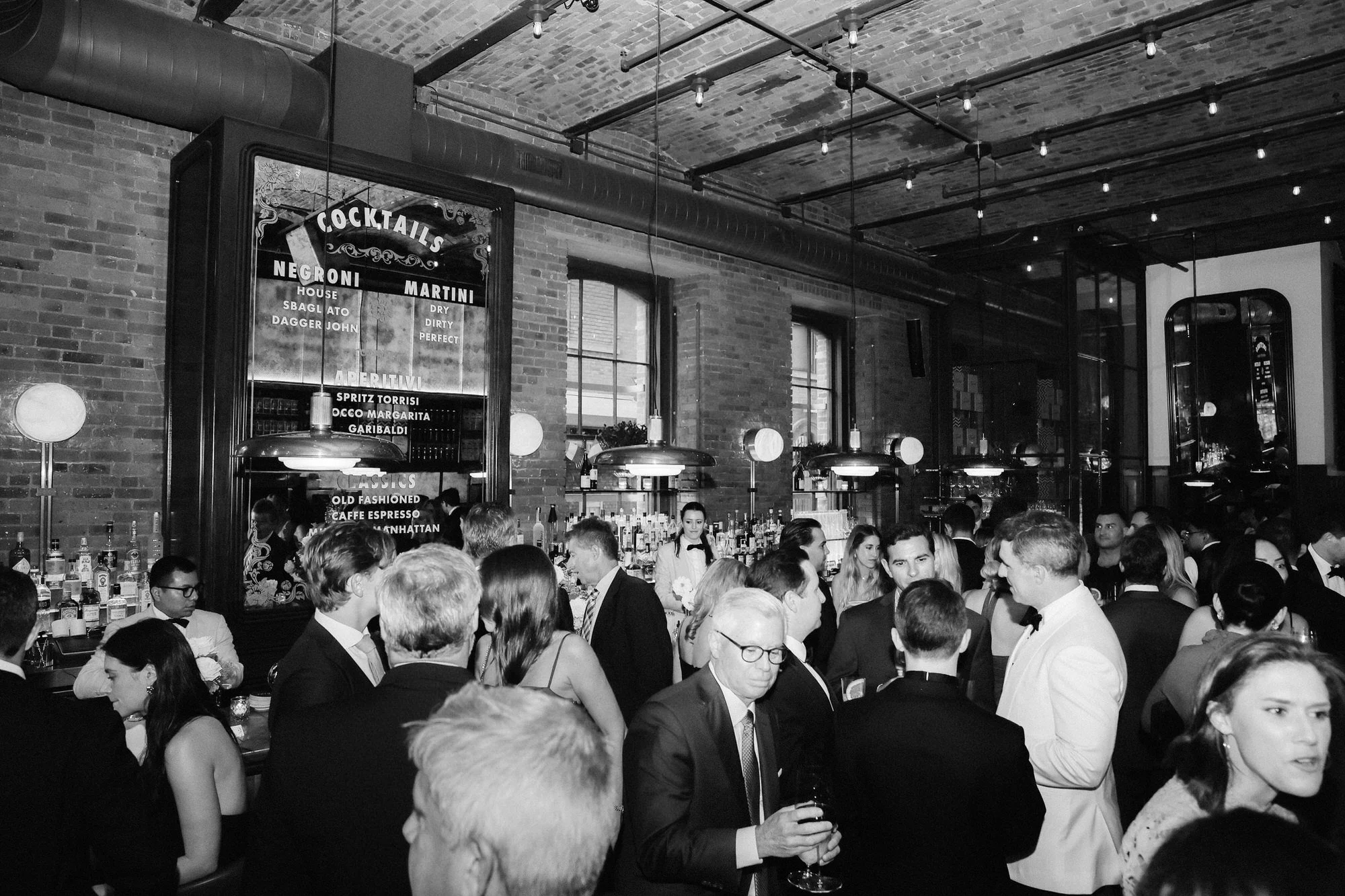 Guests mingling during cocktail hour beneath warm brick arches and vintage lighting at Torrisi in Manhattan, photographed by Jenny Fu.