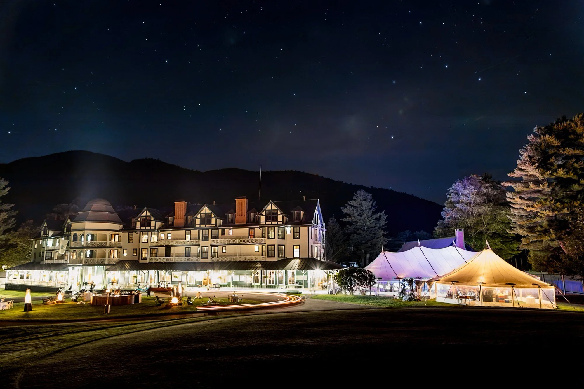 Nighttime view of the Ausable Club with tents glowing under the starry Adirondack sky