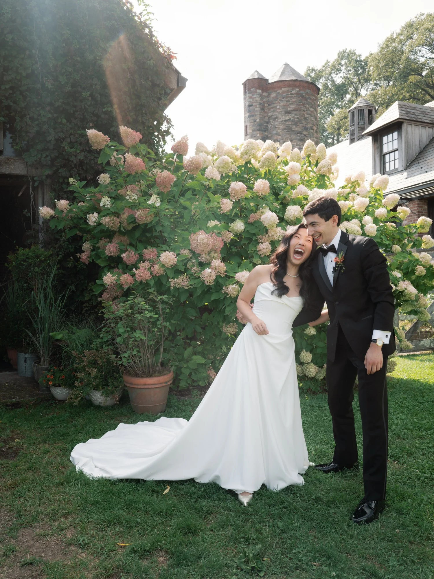 Bride and groom laughing together by the hydrangea garden with the barns behind them at Blue Hill at Stone Barns, photographed by Jenny Fu.