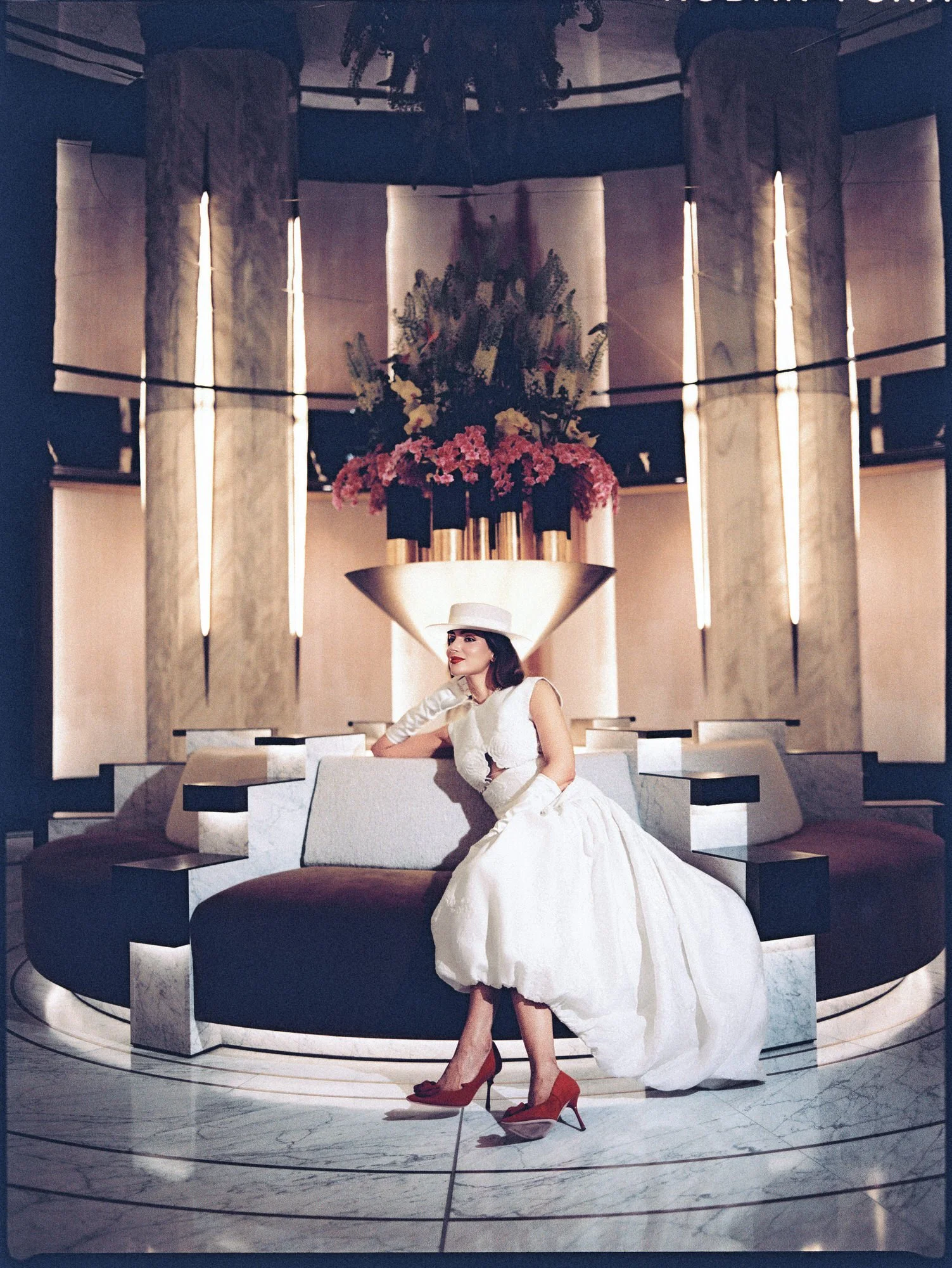 Bride seated on a round banquette beneath a floral arrangement at the Waldorf Astoria New York, photographed by Jenny Fu.