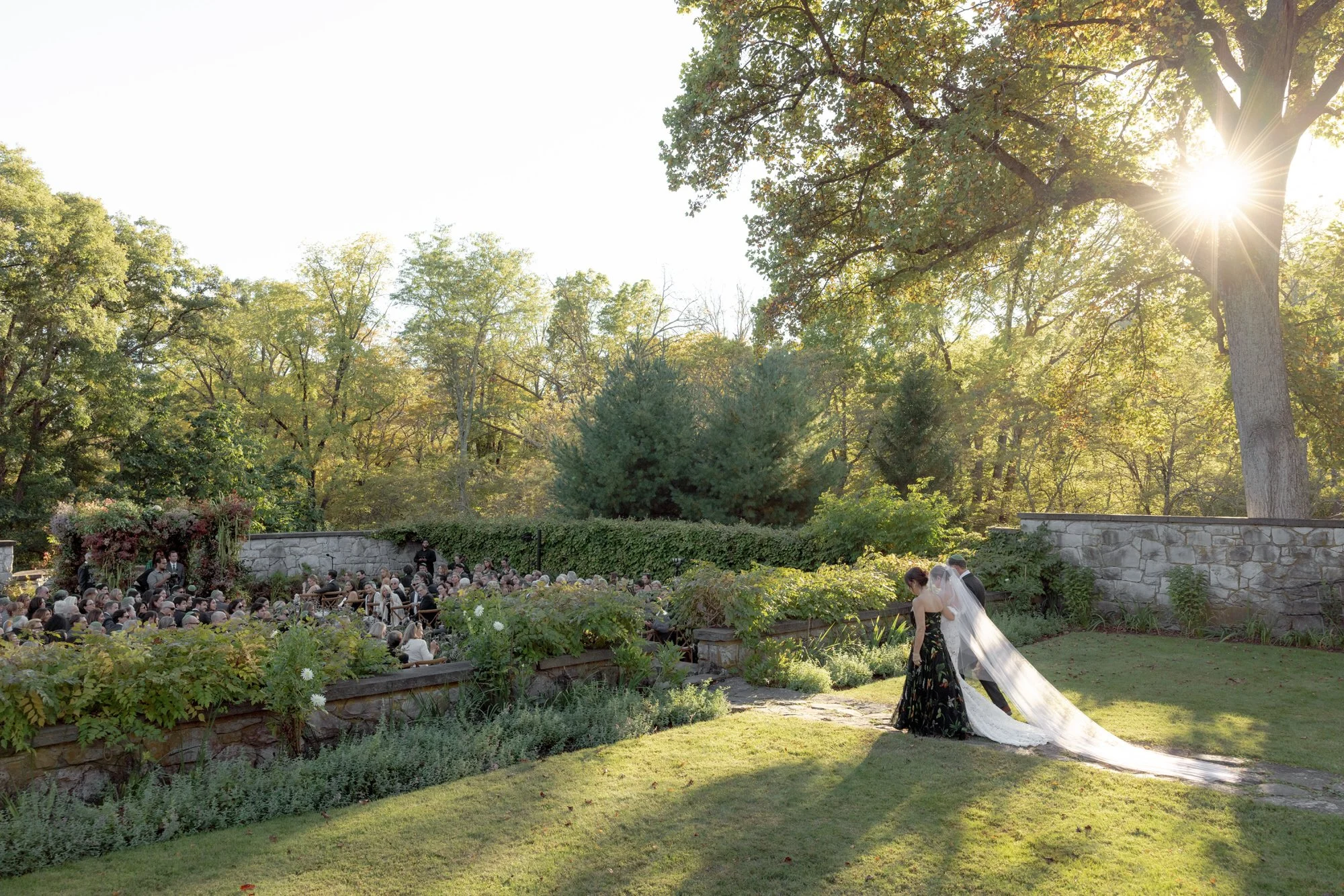 Bride making her way to the ceremony as golden sunlight filters through the trees at Troutbeck in Amenia, photographed by Jenny Fu.