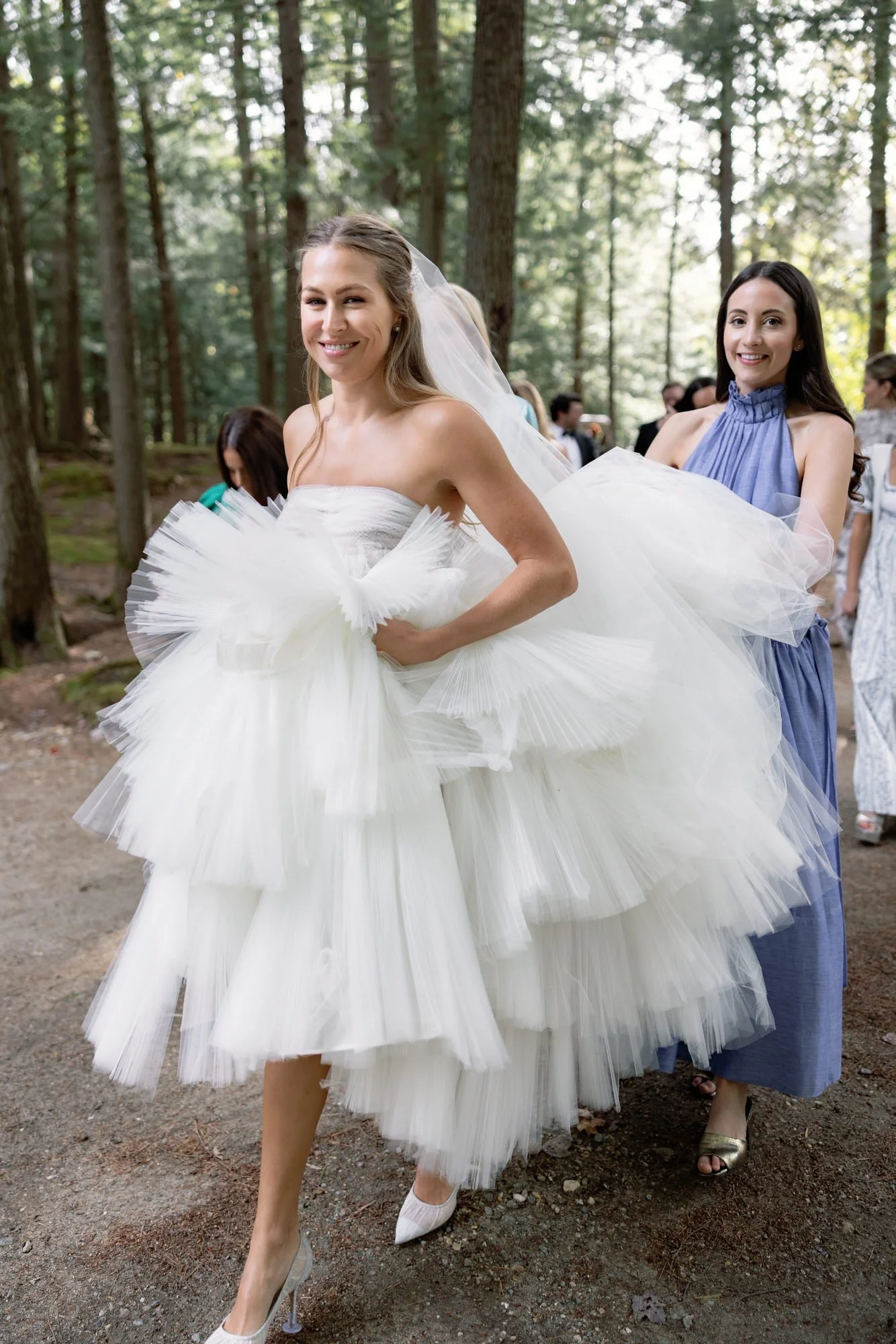 Bride in layered tulle gown smiling while walking to ceremony with bridesmaid at the Ausable Club in the Adirondacks