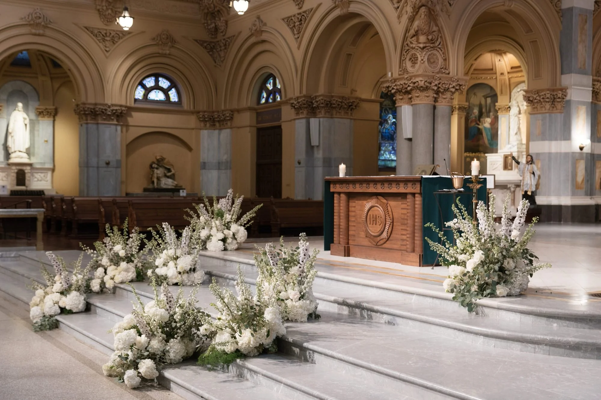 Elegant white floral arrangements cascading across the altar steps at St. Francis Xavier Church in Chelsea, photographed by Jenny Fu.