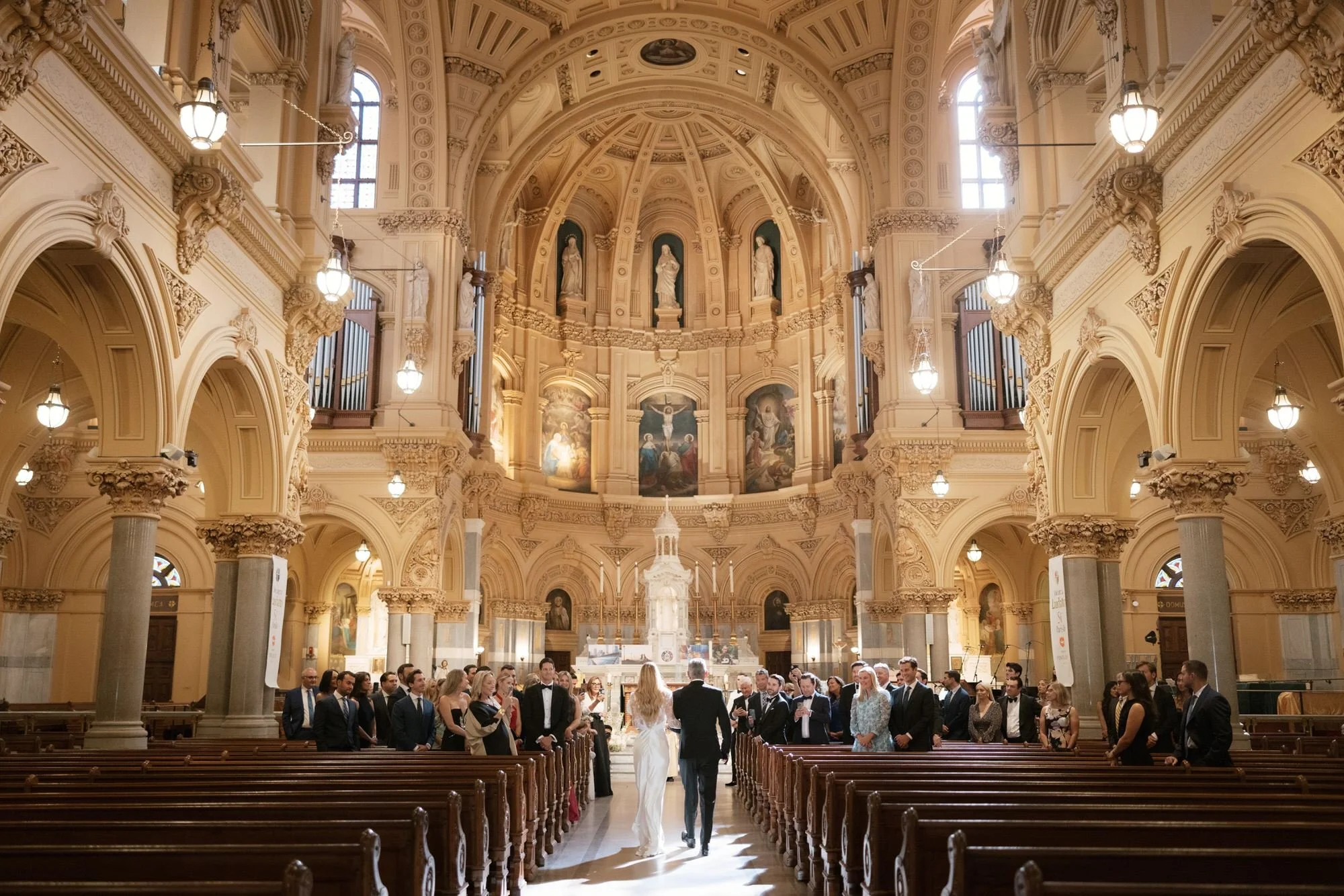 Bride and her father walking down the aisle surrounded by guests at St. Francis Xavier Church in Chelsea, photographed by Jenny Fu.