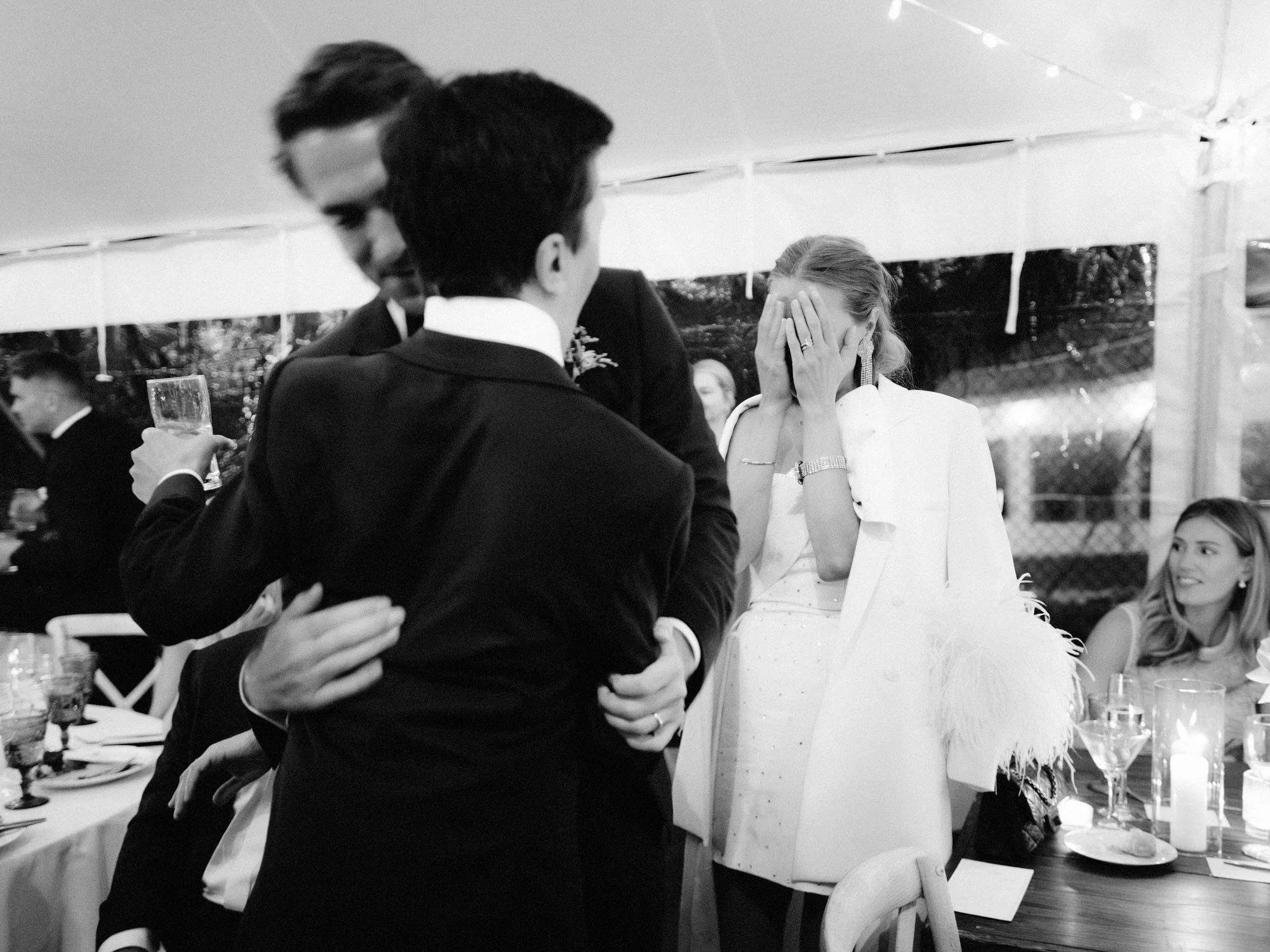 The groom hugs a friend as the bride covers her face in happy tears during the reception at the Ausable Club in the Adirondacks