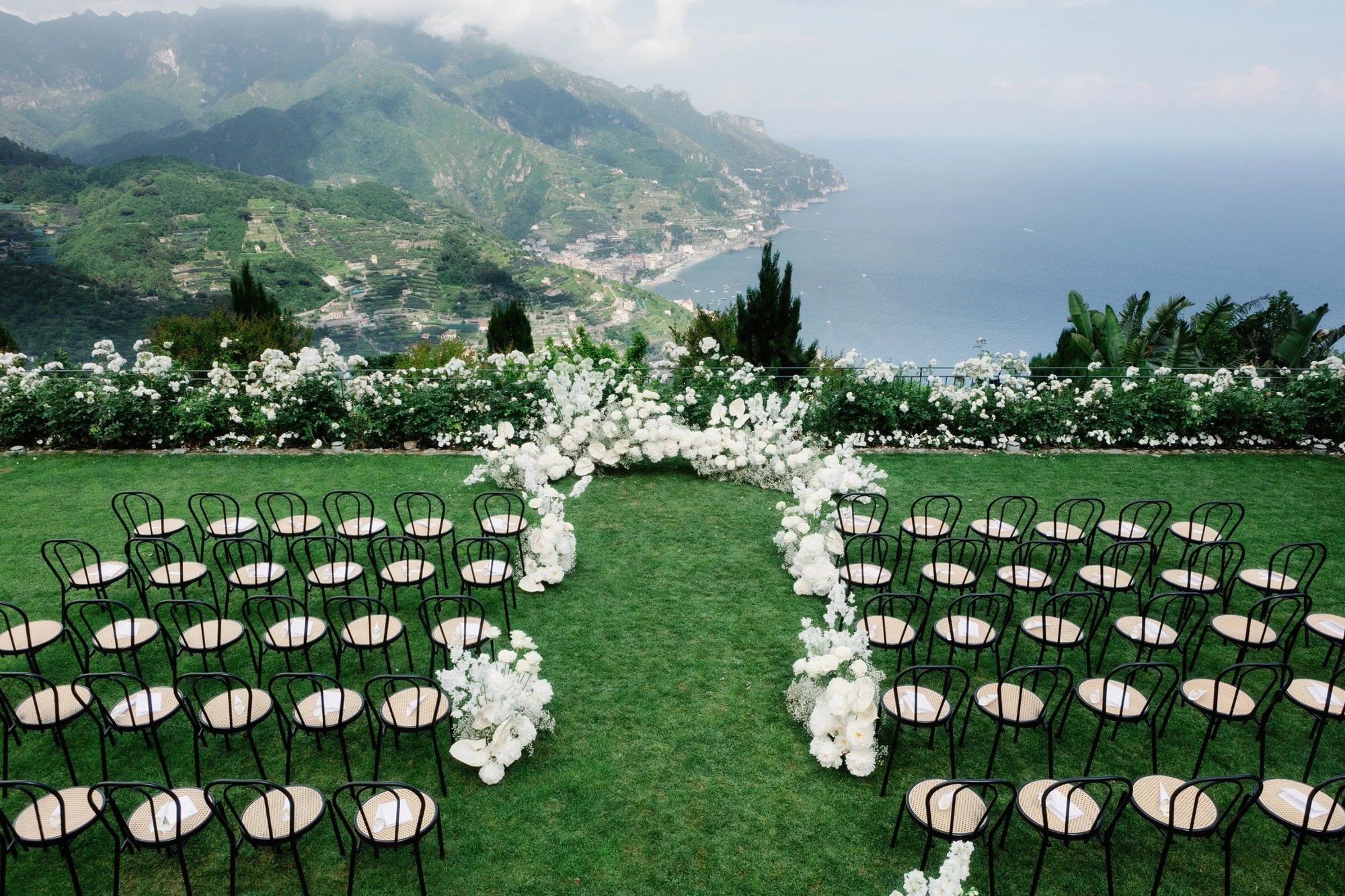 Ceremony chairs arranged in a semi-circle surrounded by white florals overlooking the Amalfi Coast at Caruso, A Belmond Hotel in Ravello, Italy, photographed by Jenny Fu.