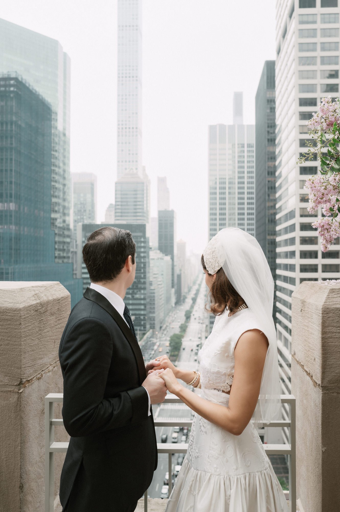 Bride and groom holding hands on a terrace overlooking Midtown Manhattan above Park Avenue skyscrapers at the Waldorf Astoria New York, photographed by Jenny Fu.