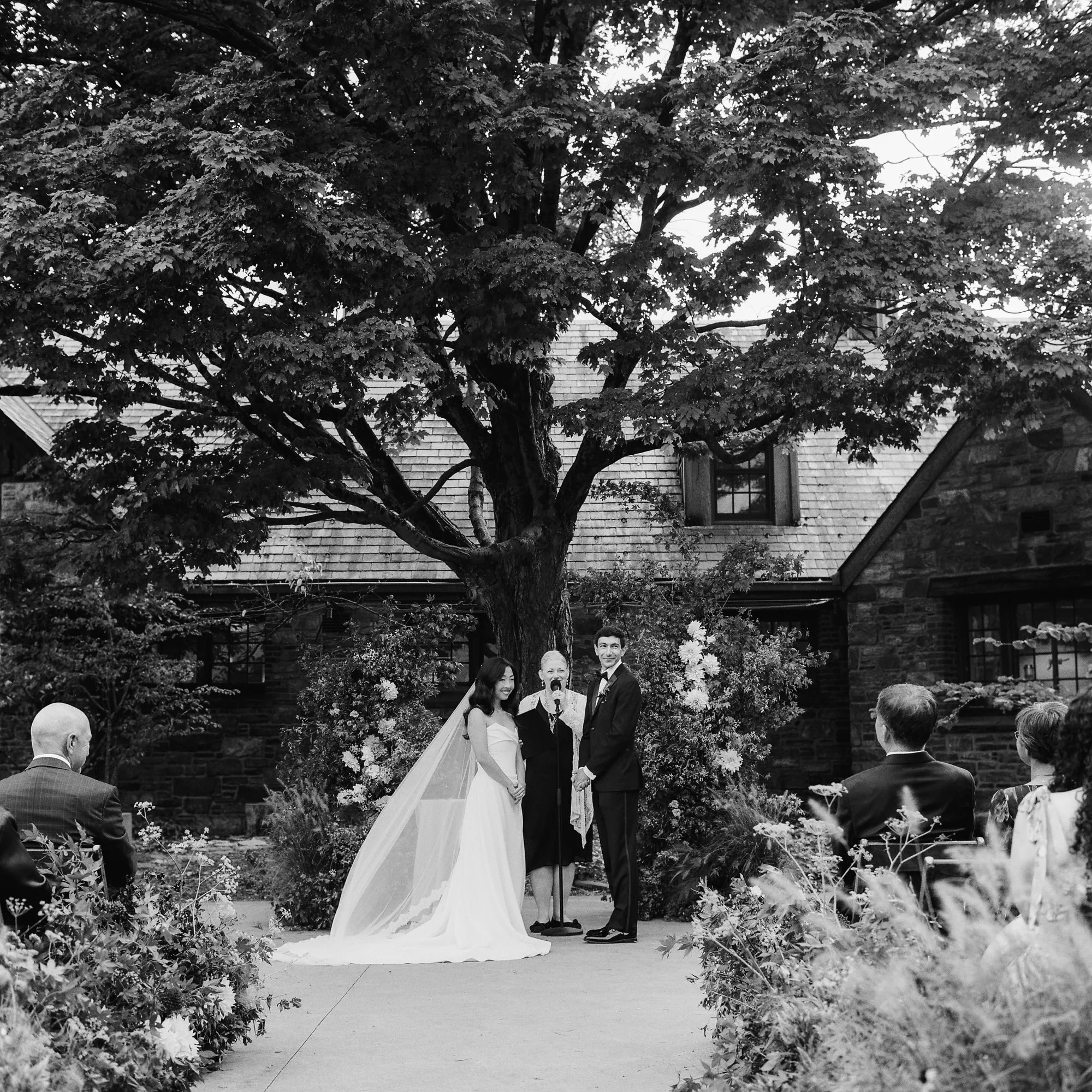 Ceremony under the maple tree with lush floral pillars in black and white at Blue Hill at Stone Barns, photographed by Jenny Fu.
