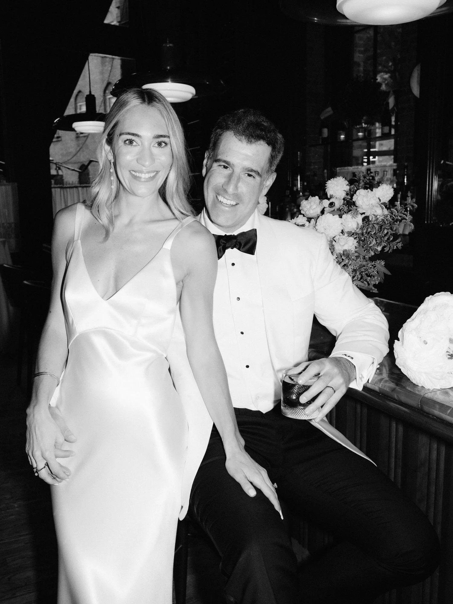 Bride and groom smiling together at the bar surrounded by soft light and florals at Torrisi in Manhattan, photographed by Jenny Fu.