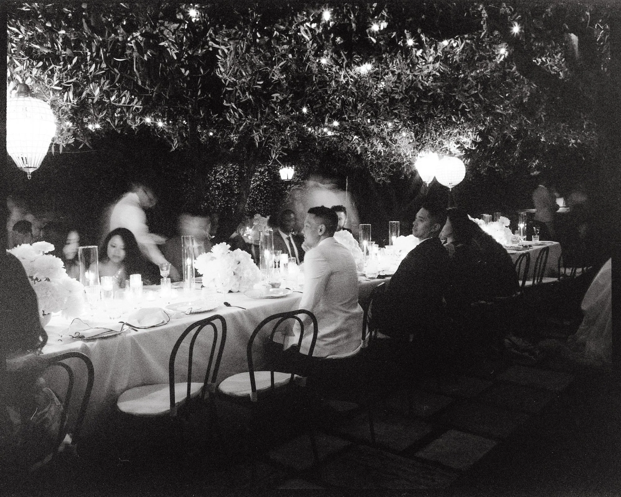 Black-and-white image of guests dining under olive trees surrounded by candlelight at Caruso, A Belmond Hotel in Ravello, Italy, photographed by Jenny Fu.