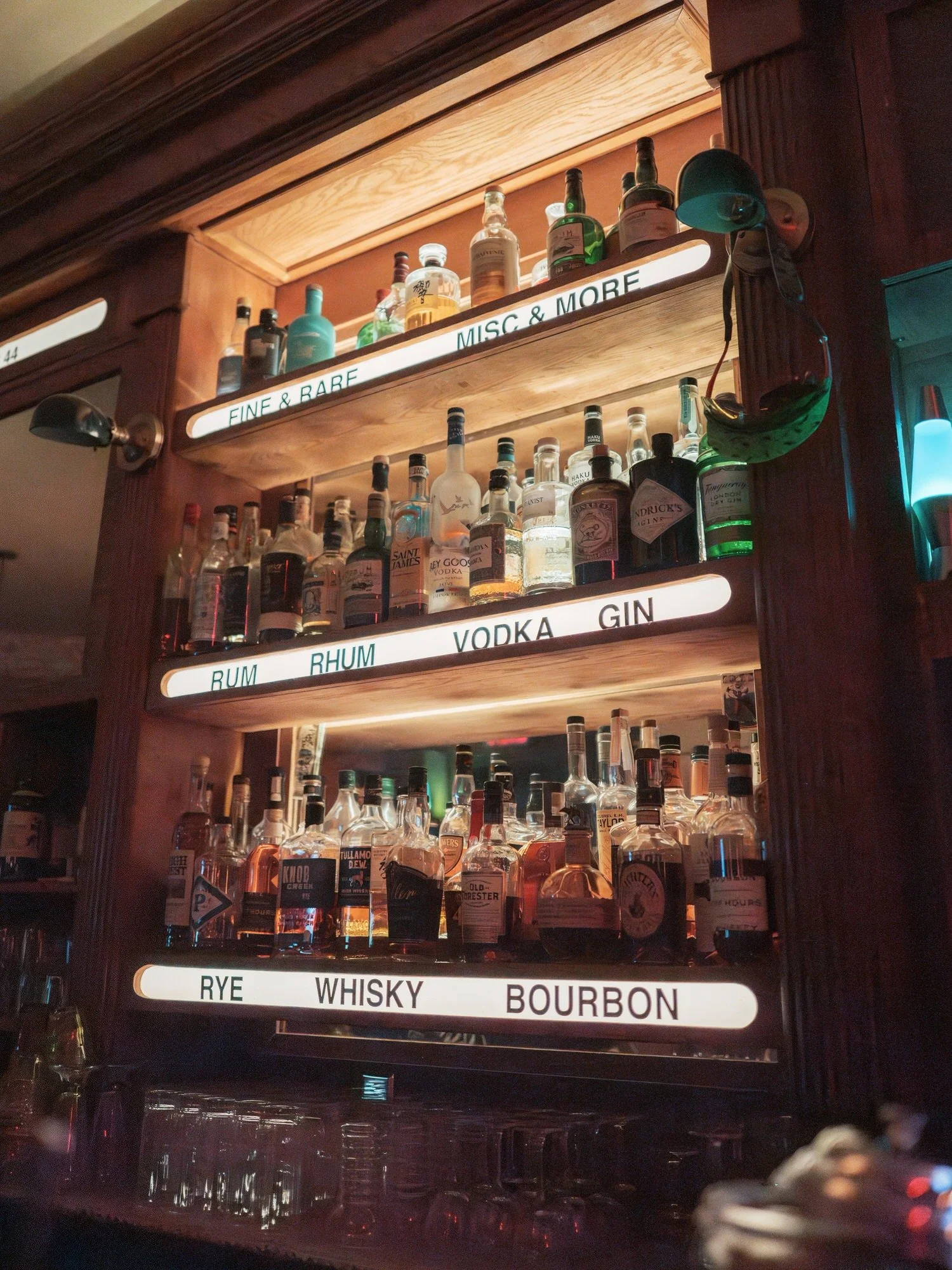 Warmly lit bar shelves showcasing fine spirits and vintage bottles during the wedding dinner at Torrisi in Manhattan, photographed by Jenny Fu.