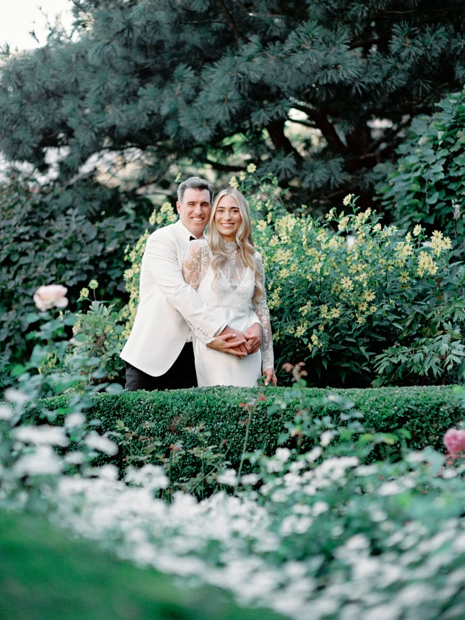 Bride and groom embracing in lush greenery surrounded by soft garden florals at Jefferson Market Garden in the West Village, photographed by Jenny Fu.