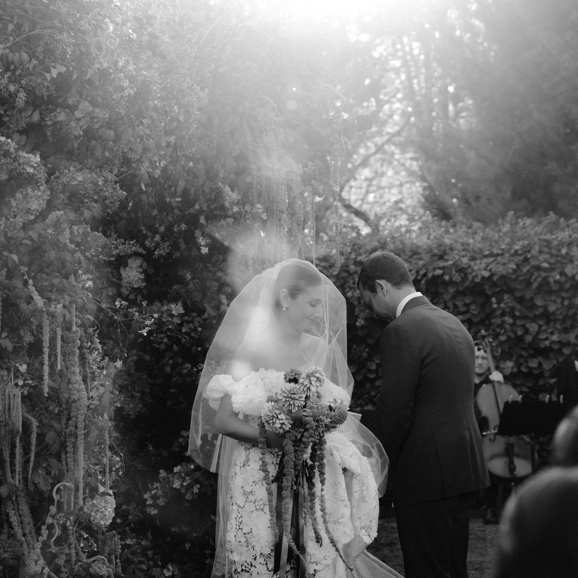 Bride and groom at the ceremony with veil and soft sunlight filtering through the garden arch at Troutbeck in Amenia, New York, photographed by Jenny Fu.
