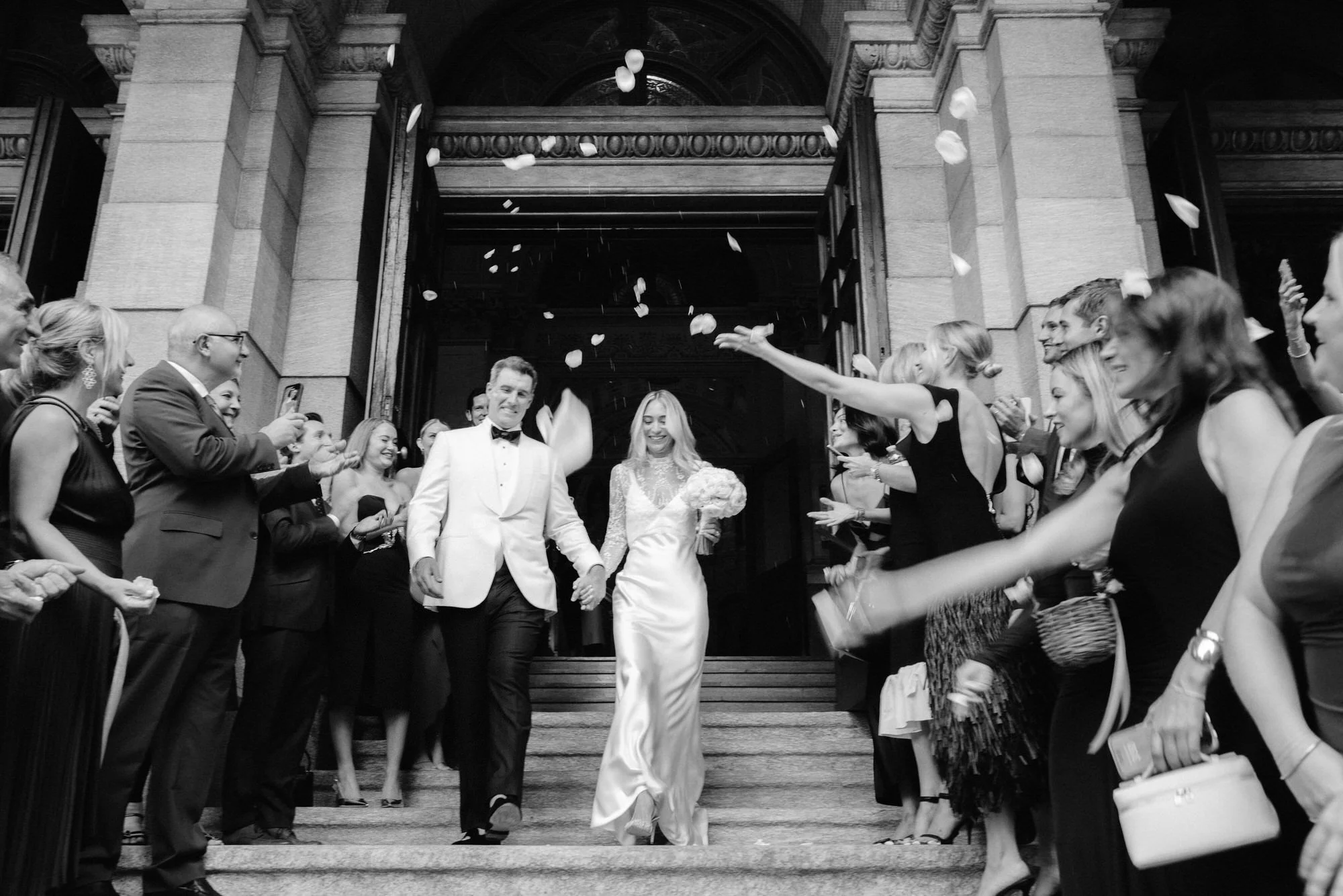 Bride and groom exiting St. Francis Xavier Church as guests shower them with rose petals, photographed by Jenny Fu.
