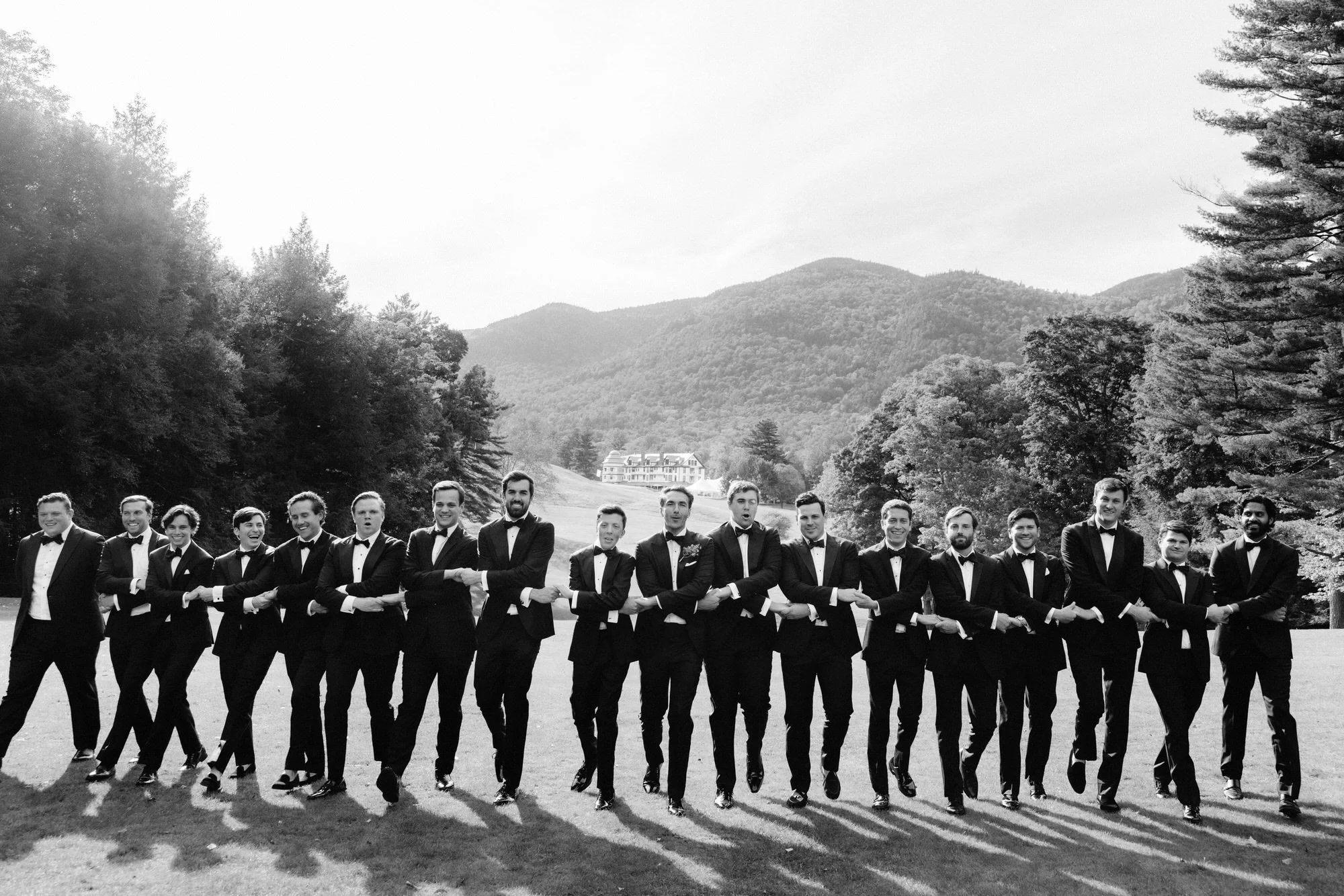 Groomsmen linking arms in a joyful group portrait at the Ausable Club with Adirondack mountains in the background