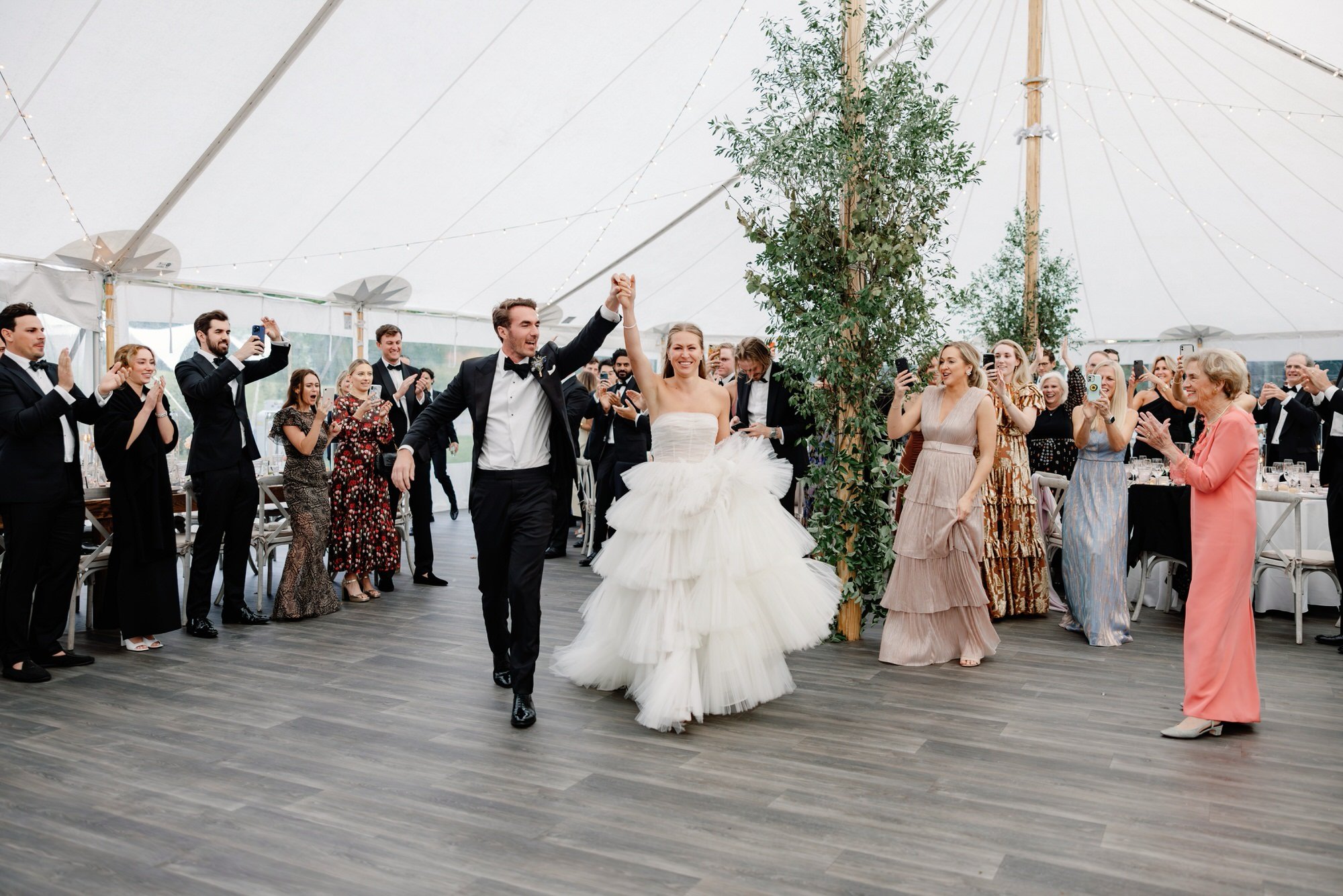 Bride and groom making a joyful grand entrance into their reception tent at Ausable Club in the Adirondacks