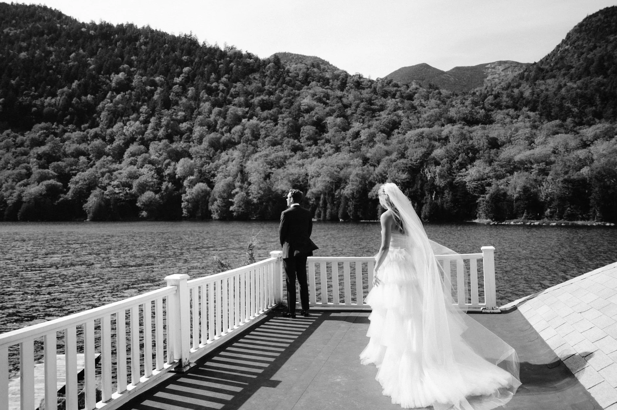 Bride in tiered tulle gown walking toward groom during first look on a lakeside deck at The Ausable Club in the Adirondacks