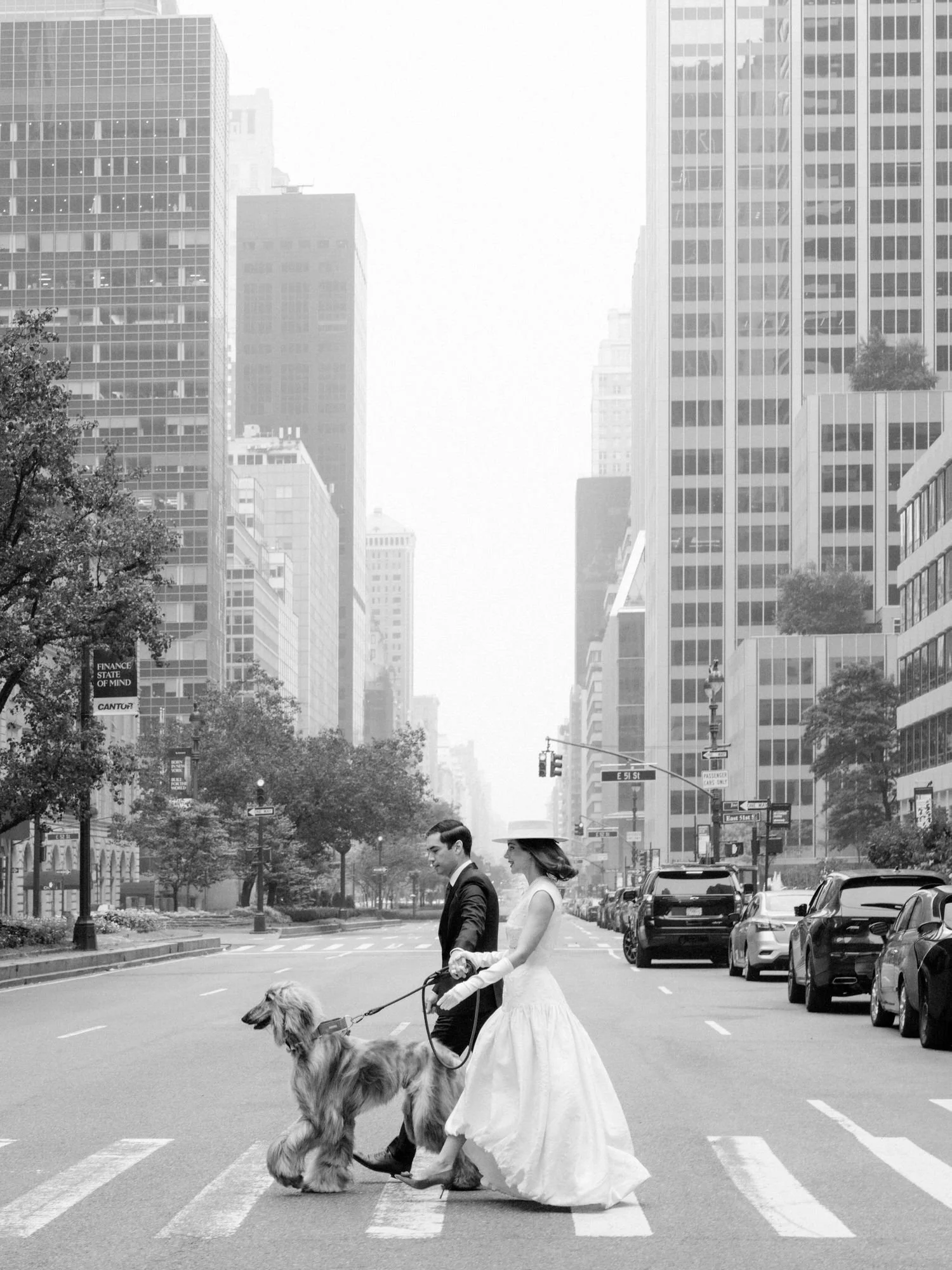 Black and white photo of the bride and groom crossing Park Avenue with their Afghan hound near the Waldorf Astoria New York, photographed by Jenny Fu.